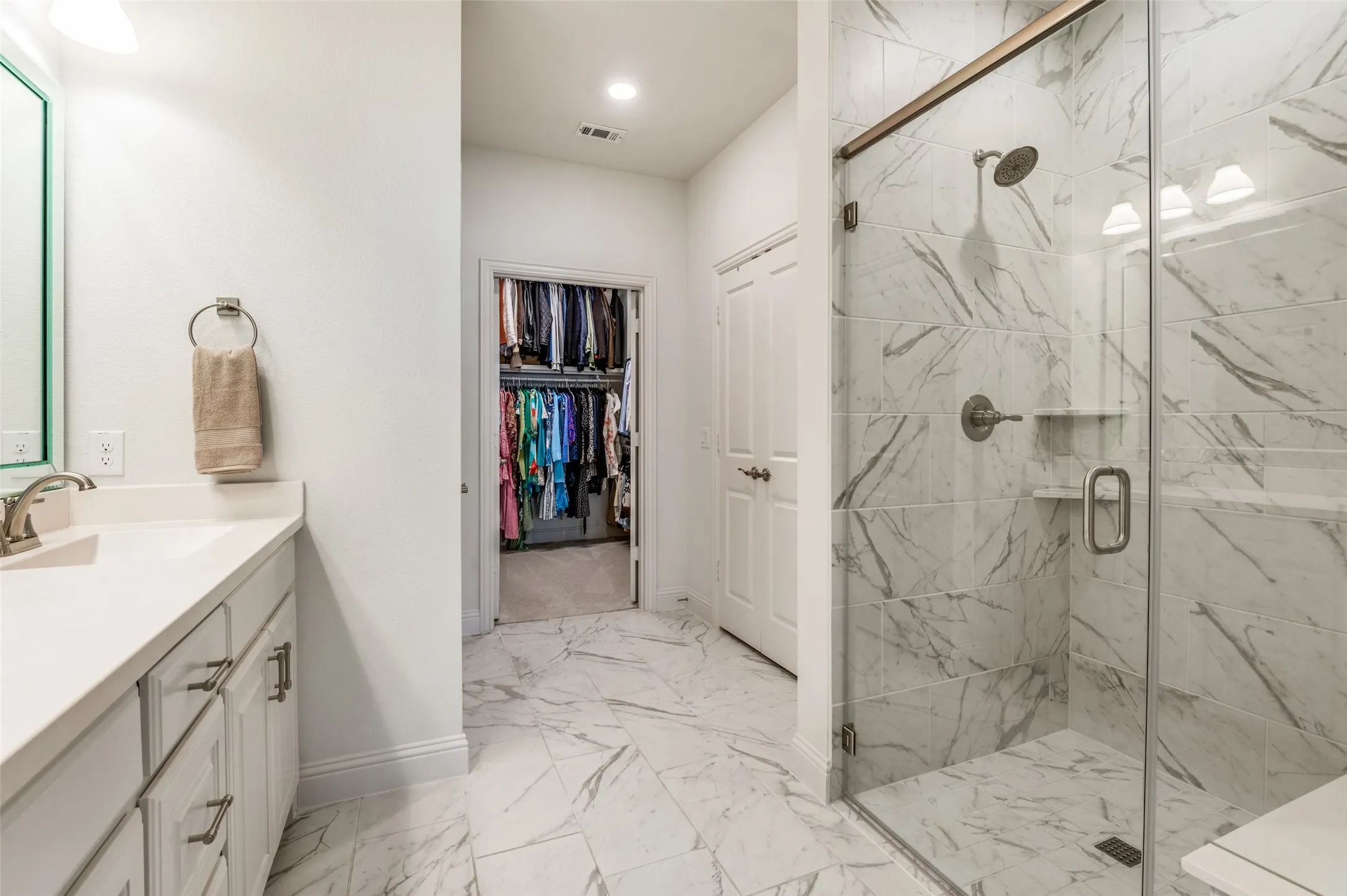 Large walk-in closet with ample hanging space and shelving, providing excellent organization and storage. Beautiful glass-enclosed shower with floor-to-ceiling marble-look tile, creating a spa-like experience in the primary bath.