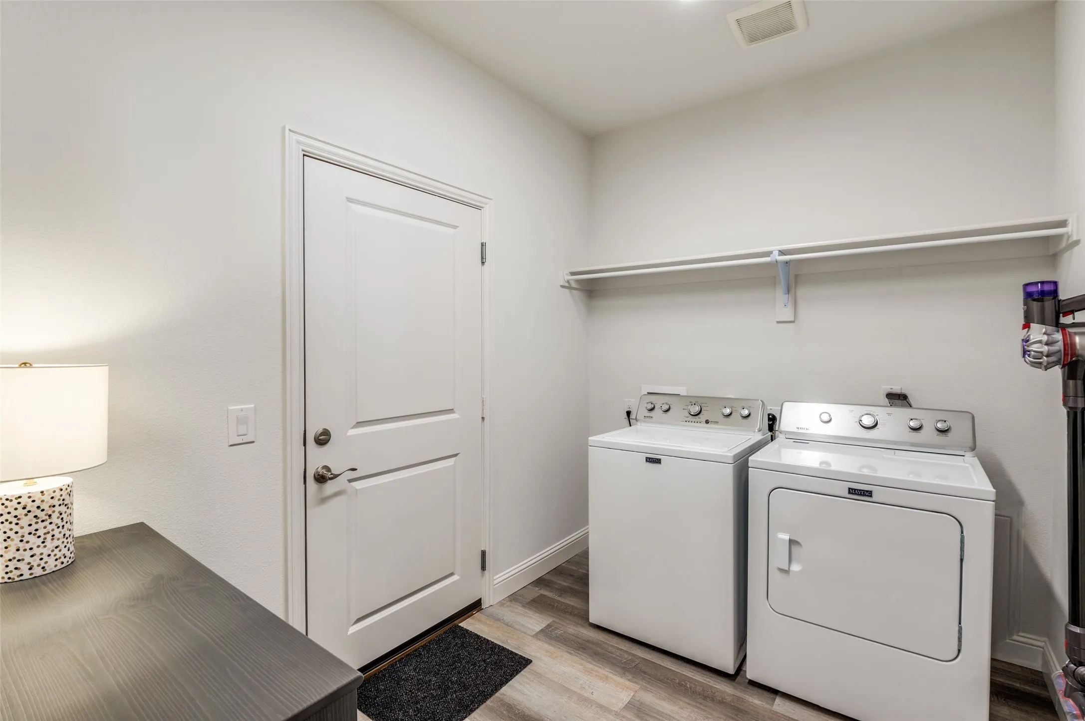 Convenient laundry room with full-size washer and dryer and additional shelving for storage and organization. Door to garage