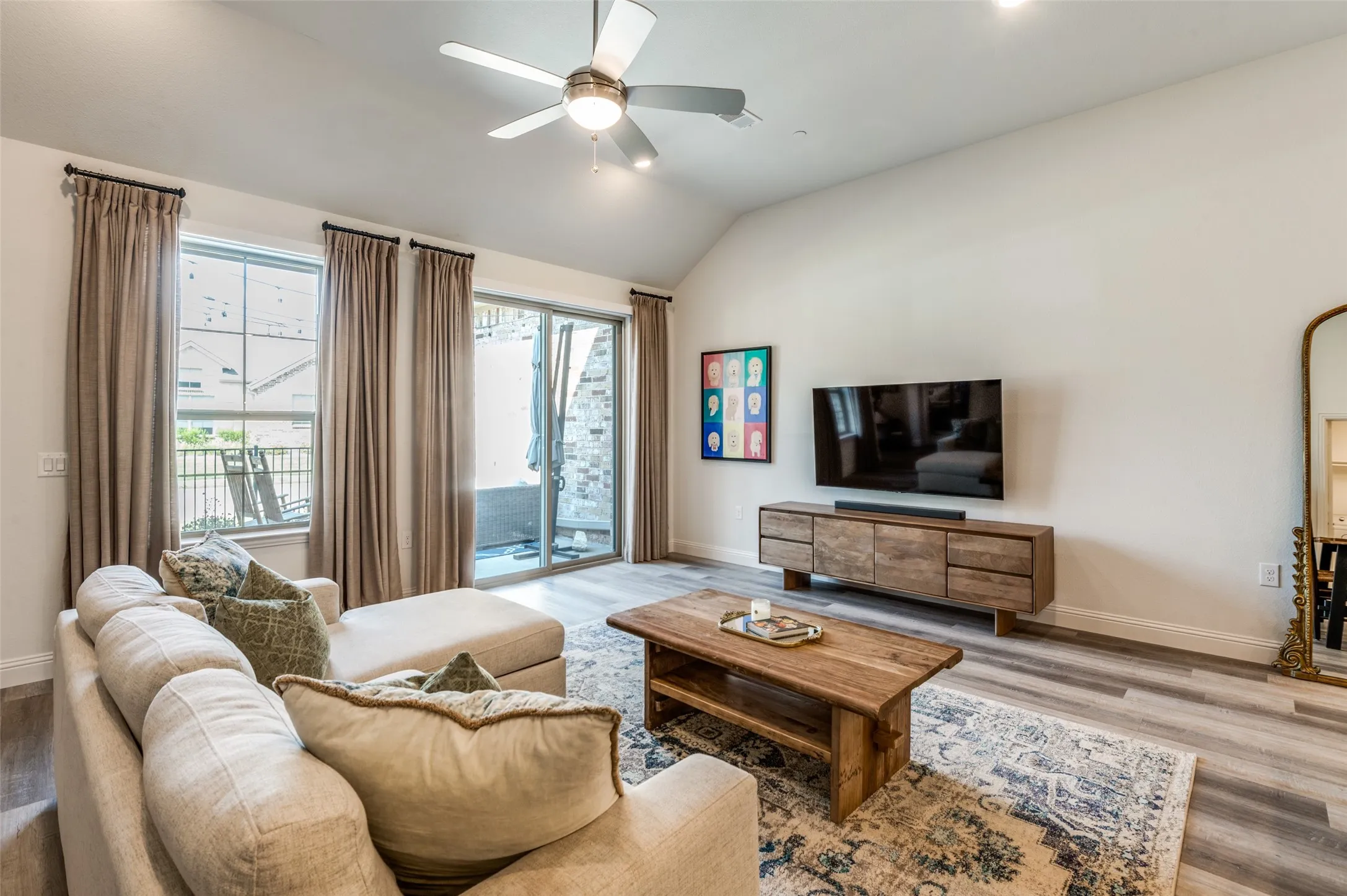 Spacious living area with vaulted ceilings, modern flooring, and large windows that fill the space with natural light. Sliding glass doors provide easy access to the patio.