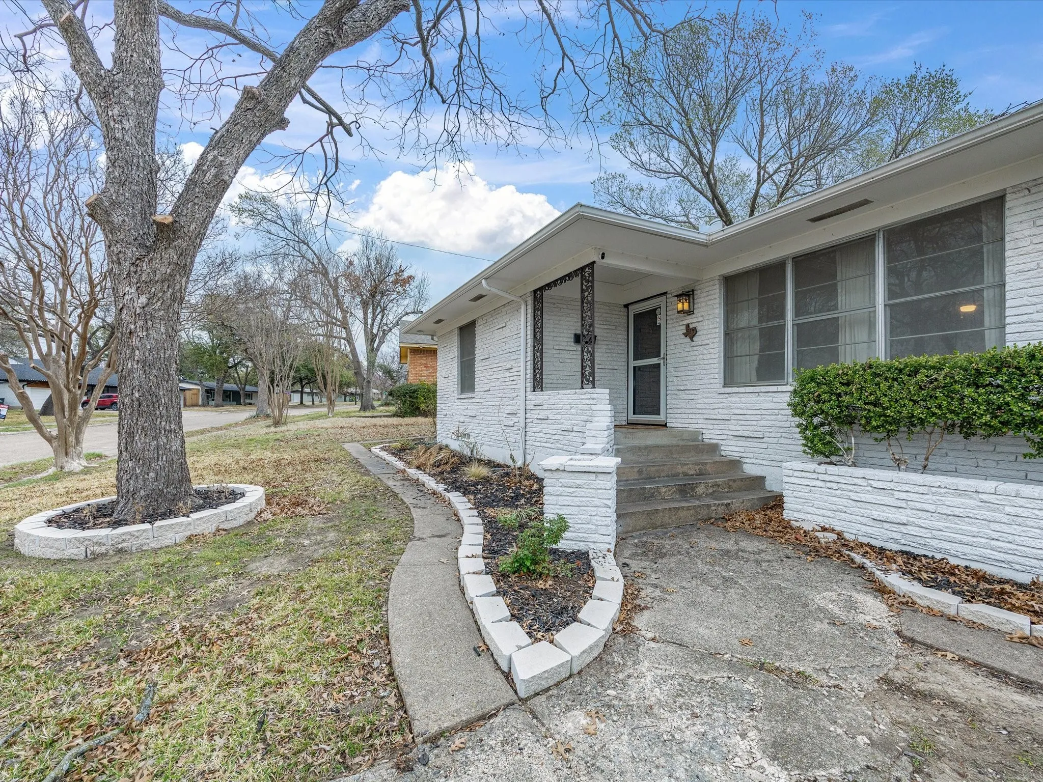 View of exterior entry with brick siding, a yard, and covered porch
