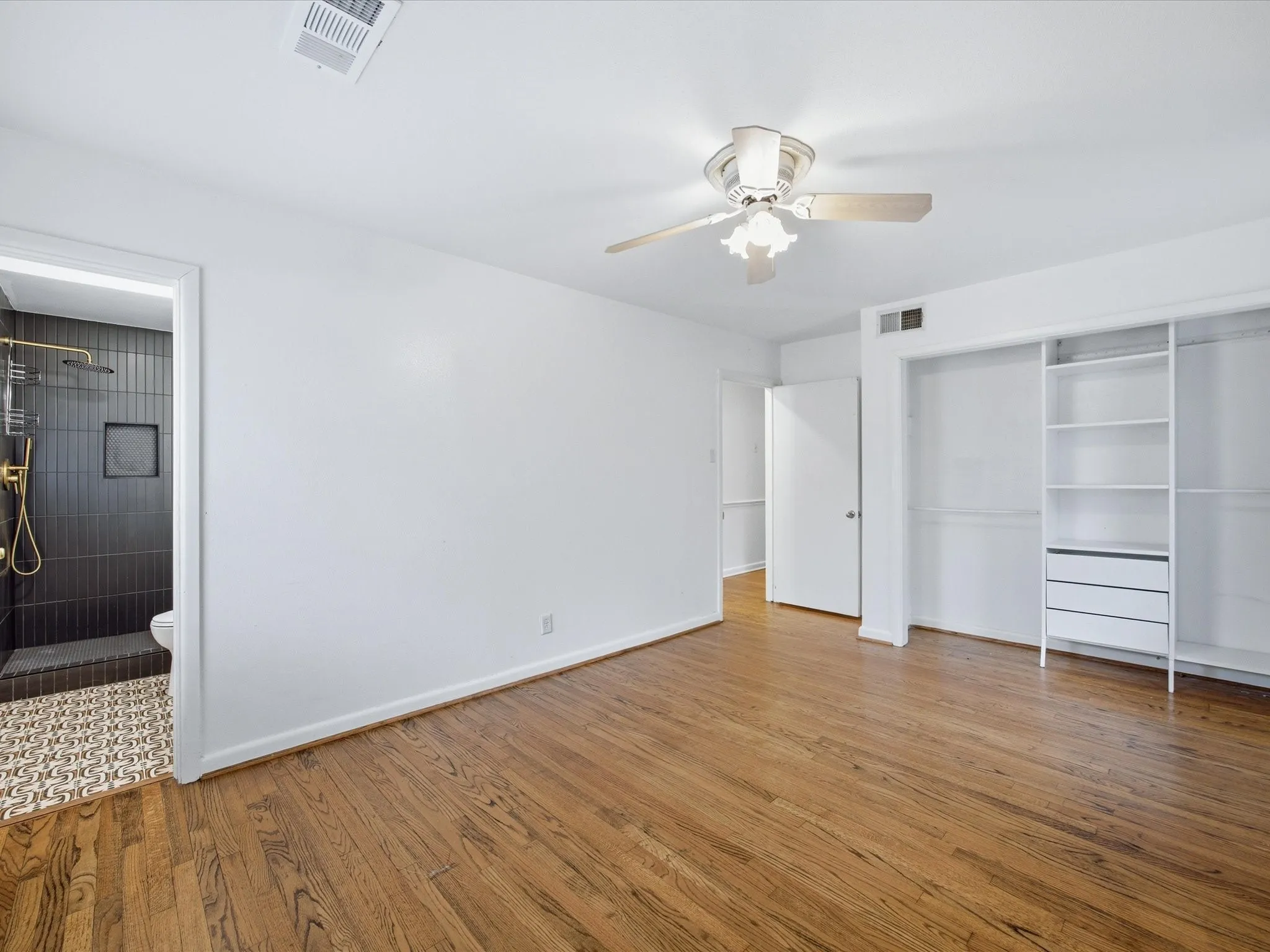 Primary bedroom with light wood-style floors, ensuite bath, ceiling fan, and a closet