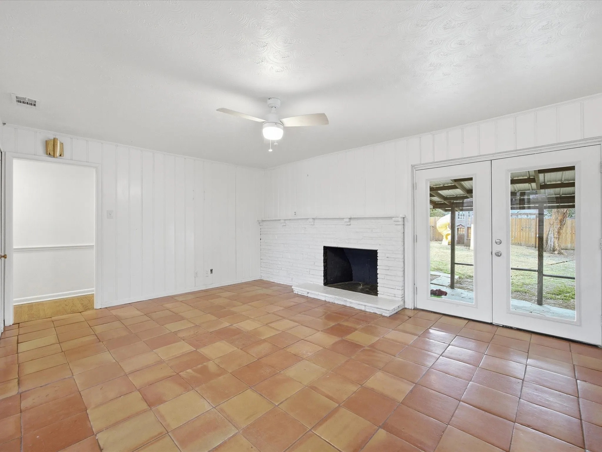 Unfurnished living room featuring ceiling fan, wooden walls, french doors, and a brick fireplace