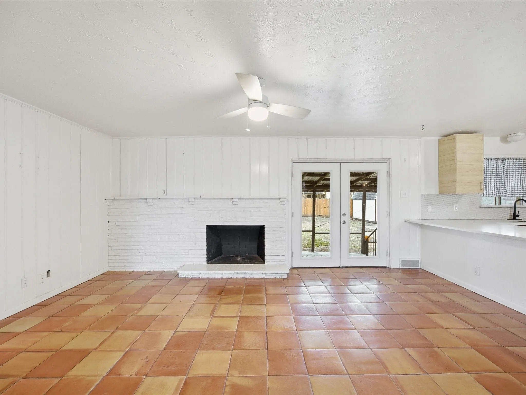 Unfurnished living room with french doors, ceiling fan, a fireplace, wooden walls, and light tile patterned floors