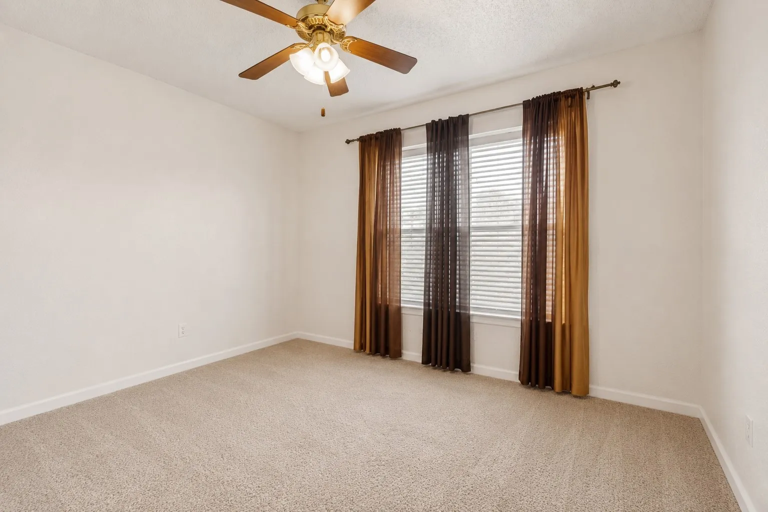Spacious room featuring neutral carpeting, light-colored walls, and a ceiling fan with integrated lighting