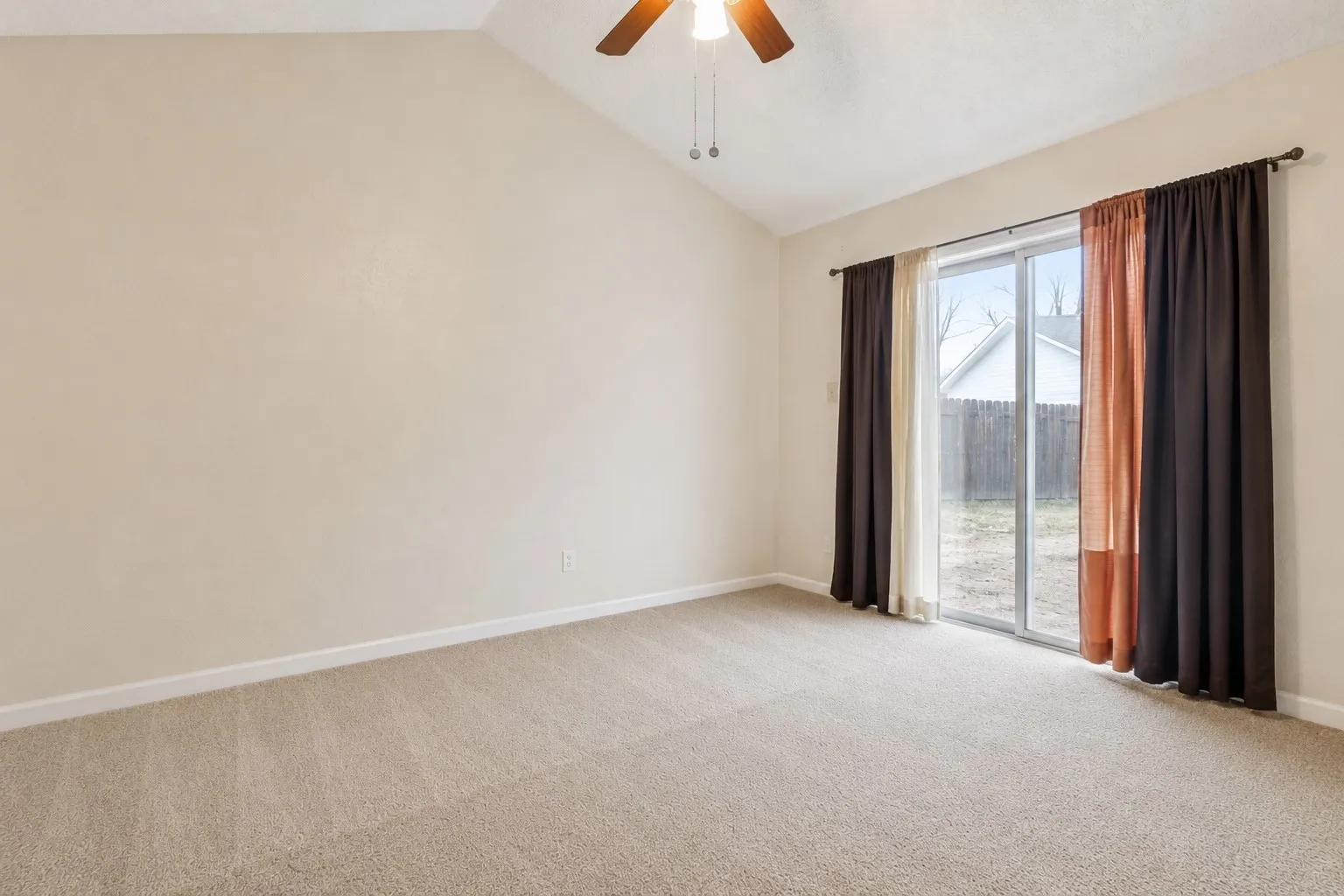 Spacious room featuring vaulted ceilings, neutral-toned carpeting, and a ceiling fan with light fixture
