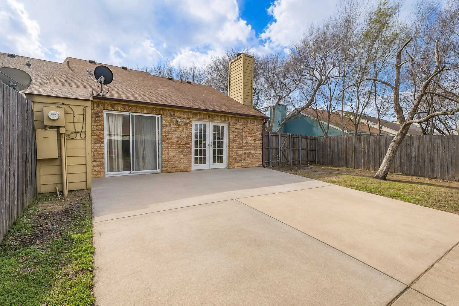 Expansive concrete patio with direct access to interior spaces through a sliding glass door and French doors