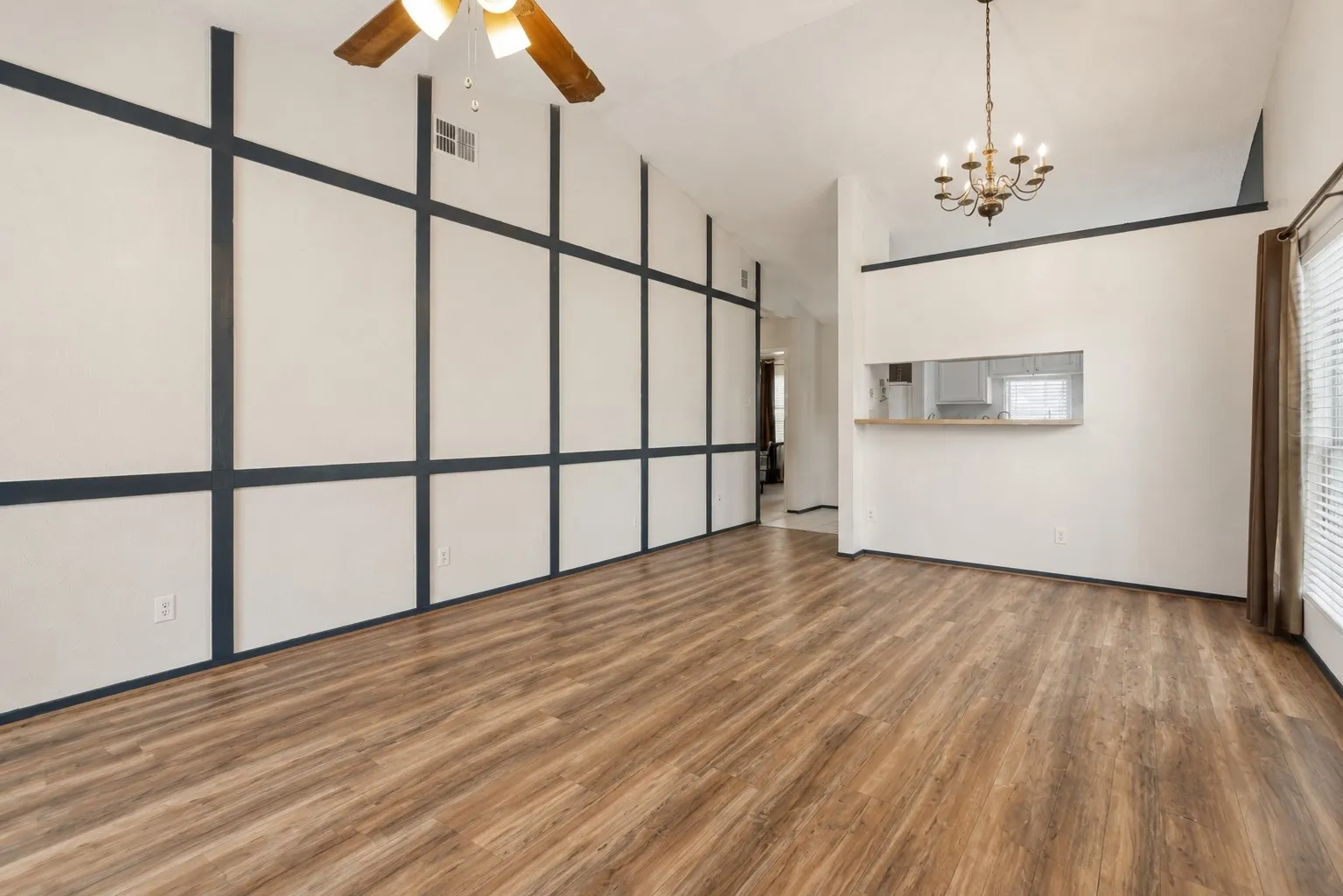 Spacious living area featuring wood-finish flooring, a vaulted ceiling, and an accent wall with dark trim