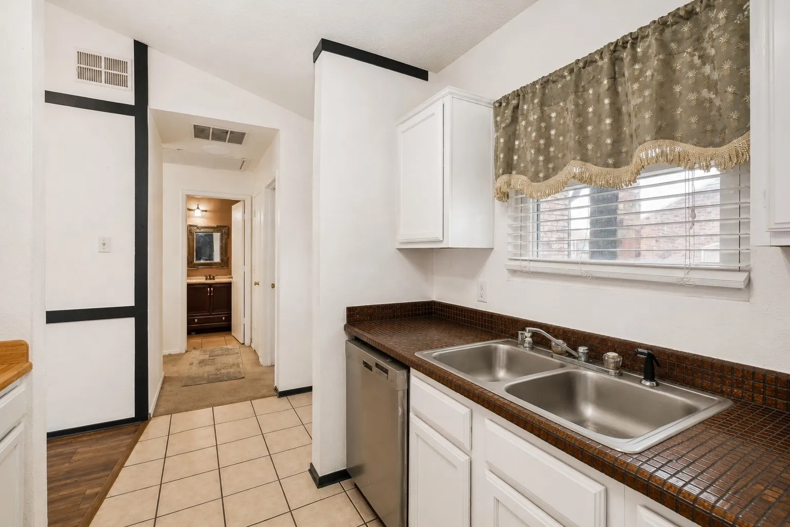 Kitchen featuring a stainless steel double basin sink, white cabinetry, and mosaic tile countertops