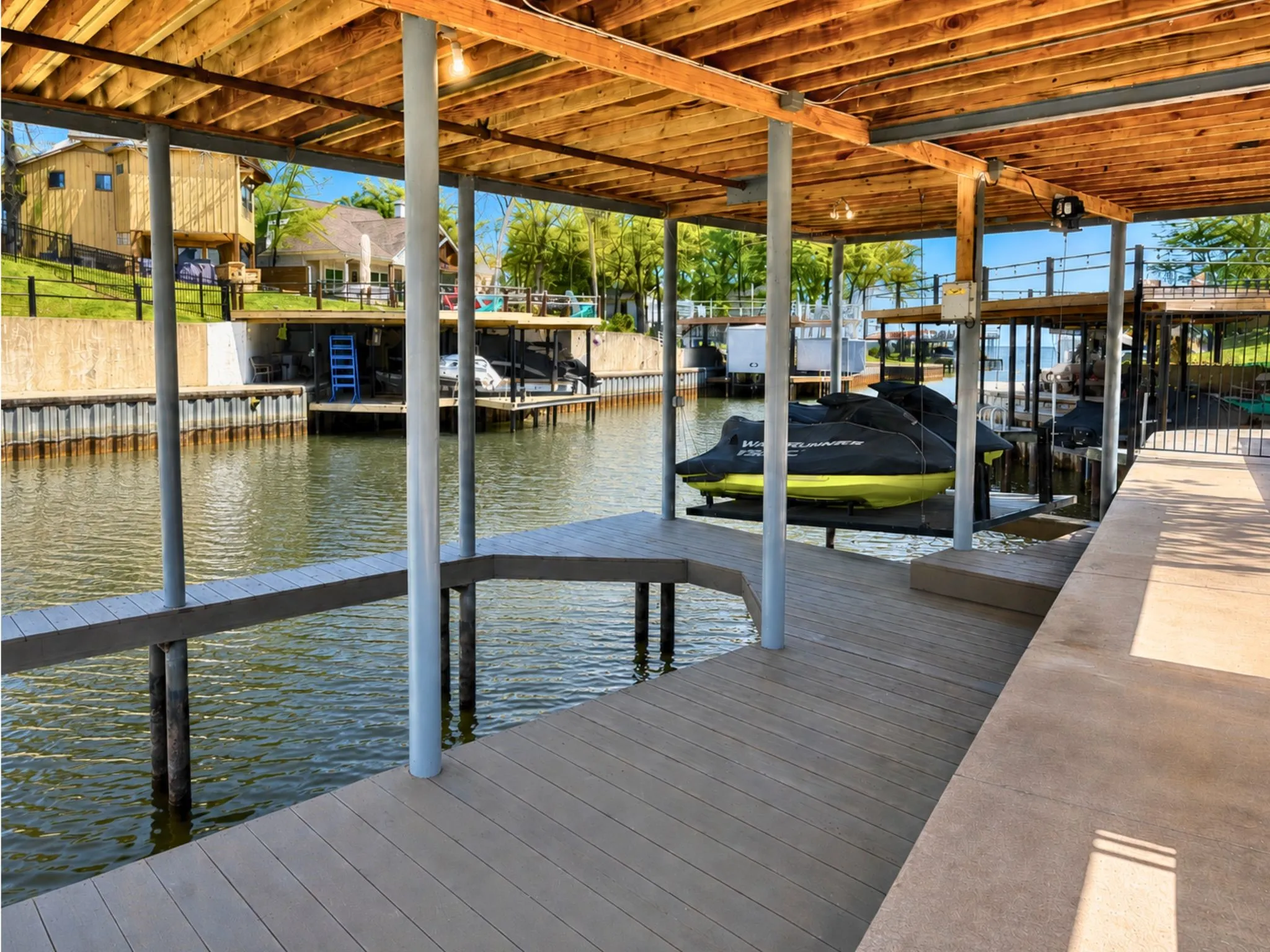 Covered boat dock featuring multiple slips, composite decking, built-in personal watercraft lifts, and a wooden ceiling structure