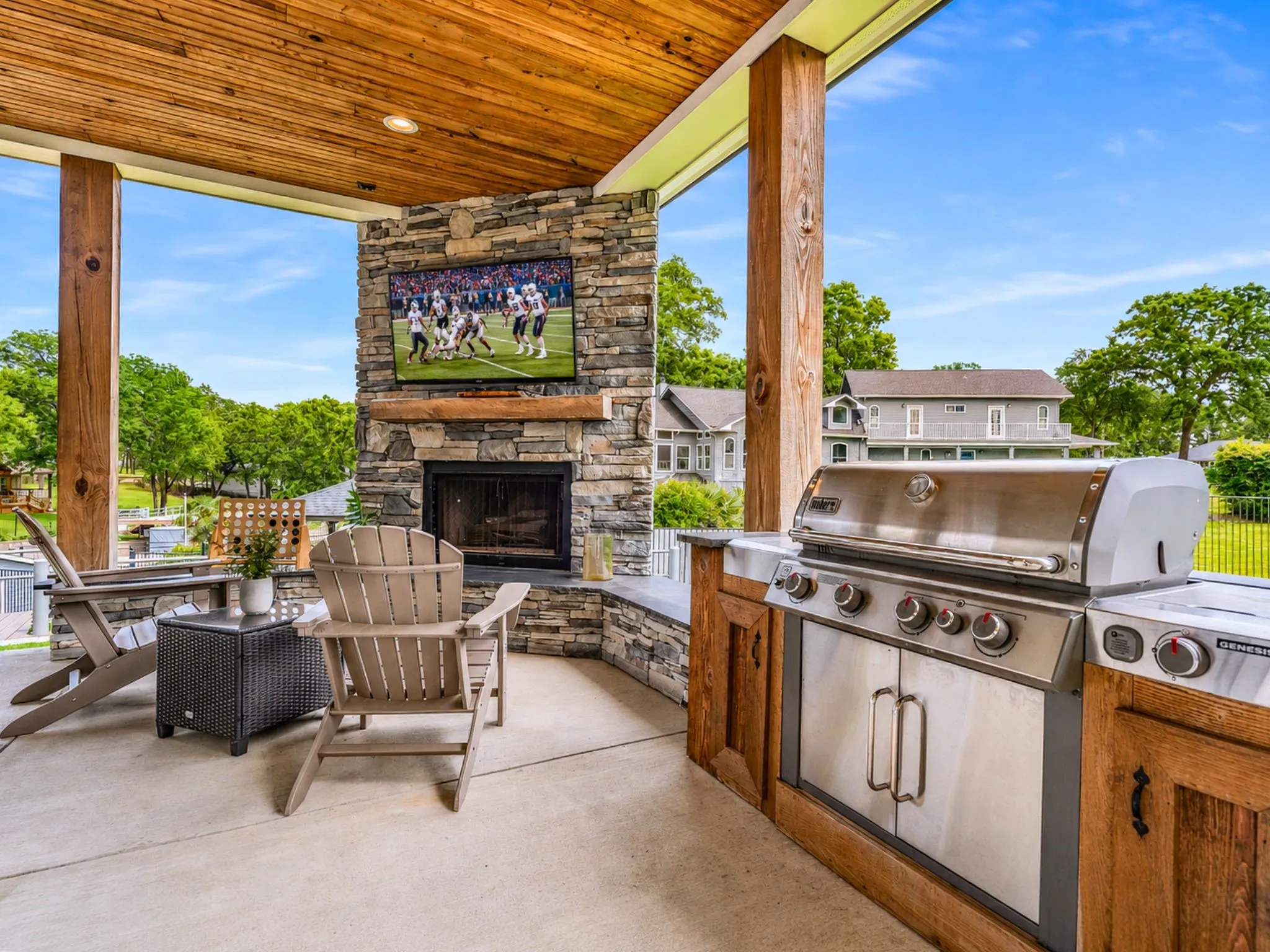Covered outdoor patio featuring a wood-panel ceiling, stone-clad fireplace, integrated outdoor kitchen with a built-in grill, and wood support beams