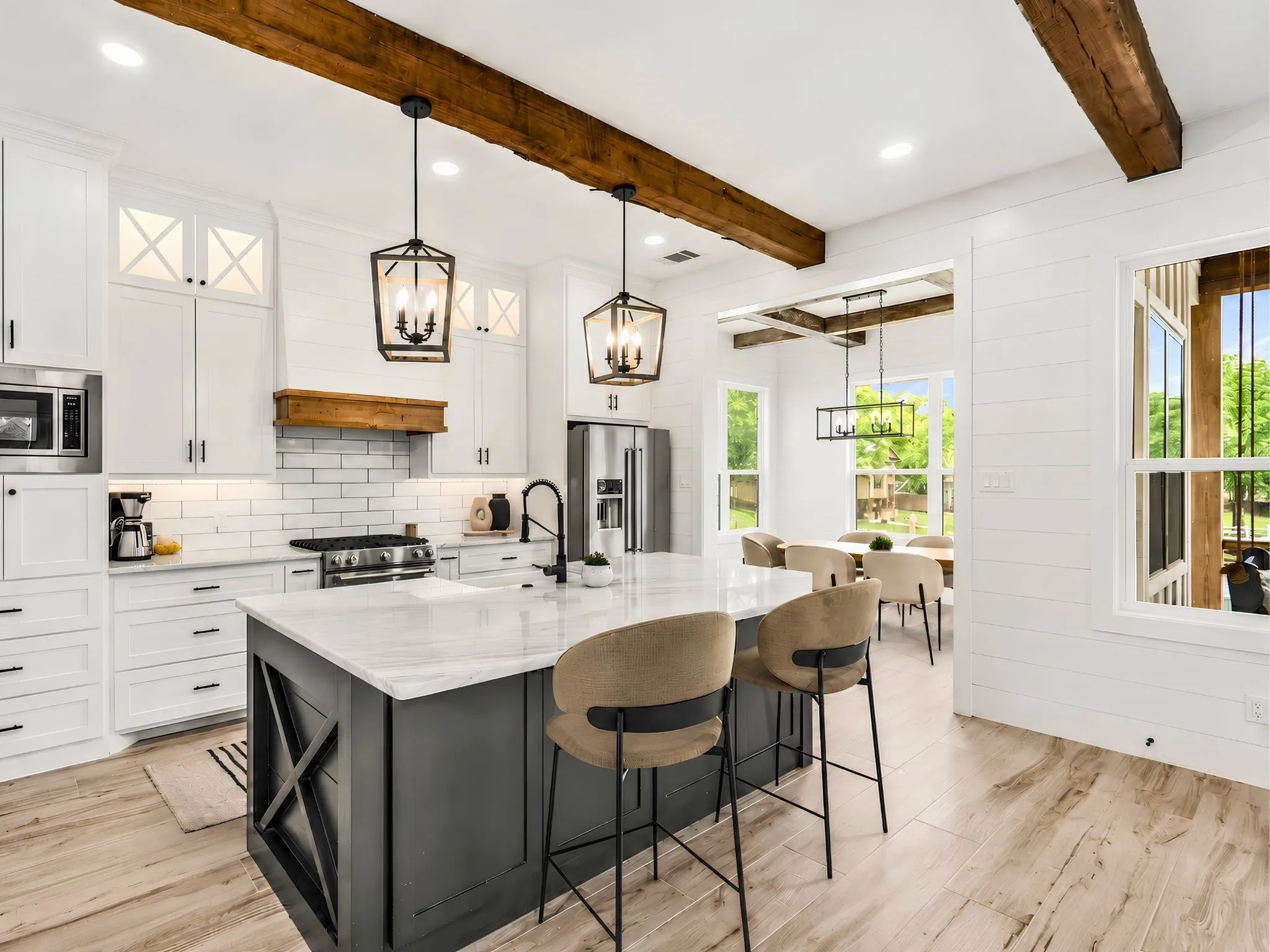 Kitchen featuring a large island with a stone countertop, wood-finish flooring, white shaker cabinetry, exposed wood ceiling beams, and stainless steel appliances