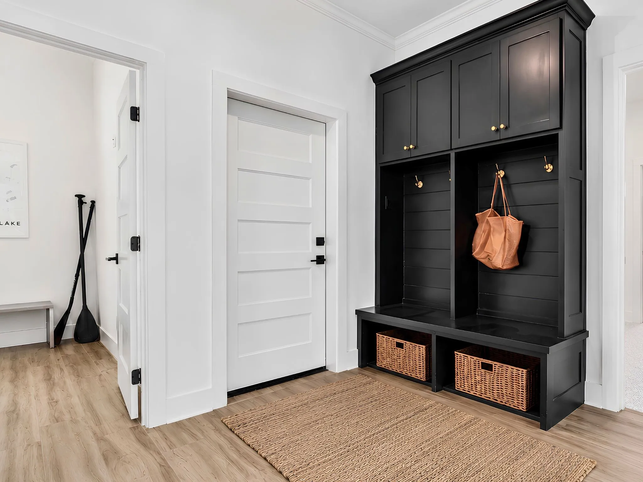 Built-in black mudroom storage unit featuring upper cabinetry, gold-toned hooks, and lower storage cubbies