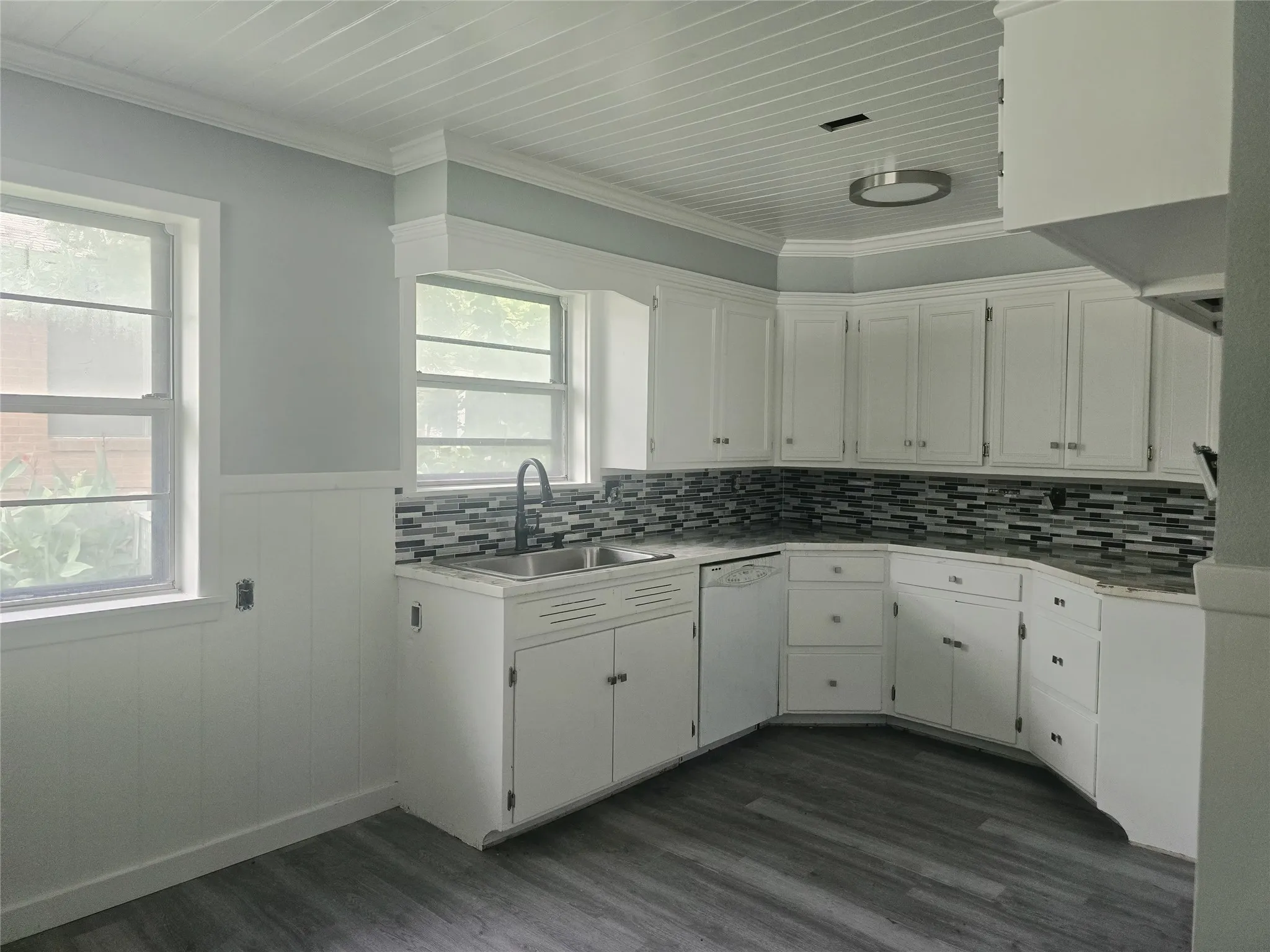 Kitchen featuring white cabinetry, a multi-tone tile backsplash, and wood-finish flooring. Updated.