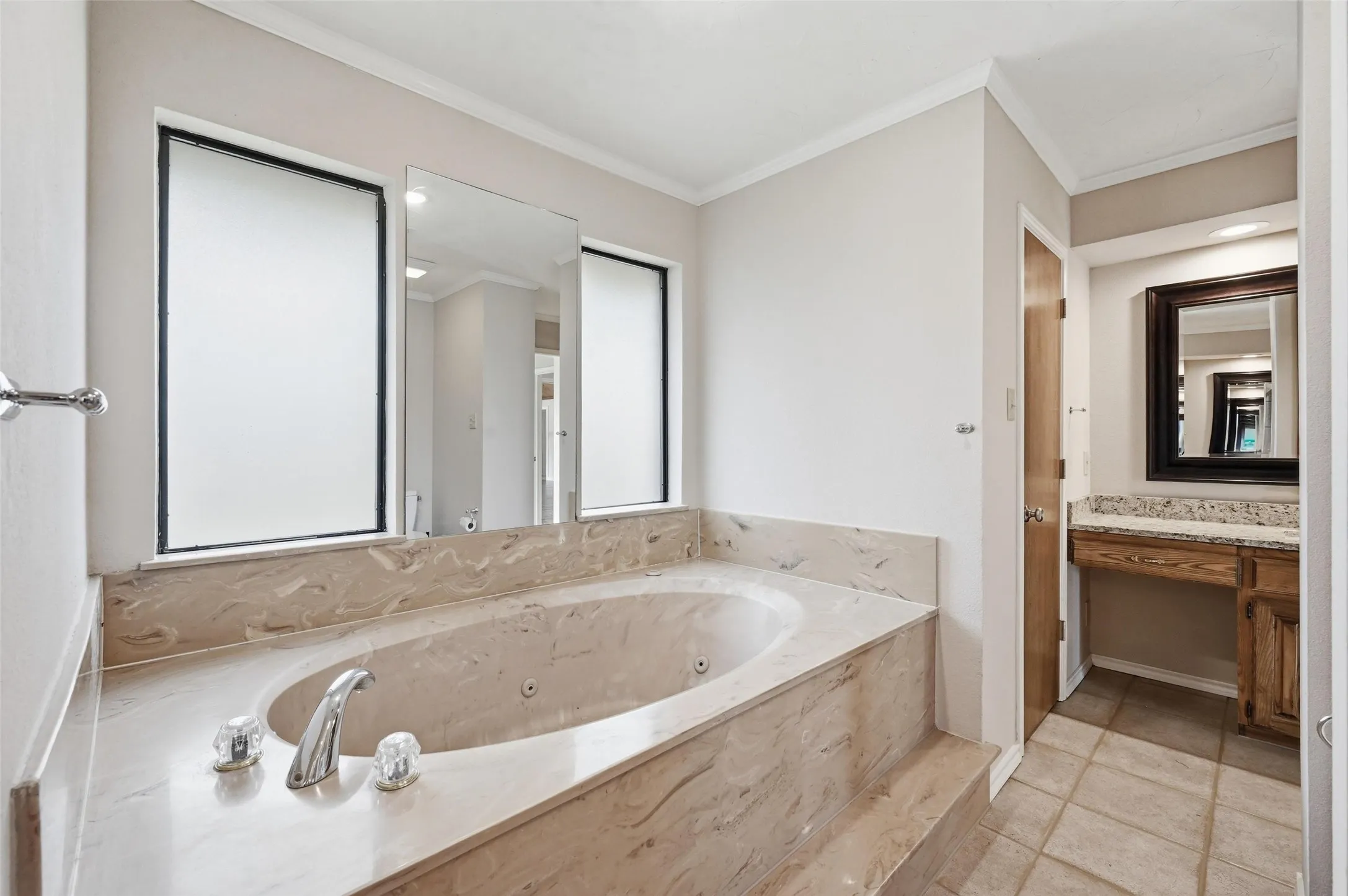 Full bathroom featuring vanity, a jetted tub, ornamental molding, and light tile patterned floors