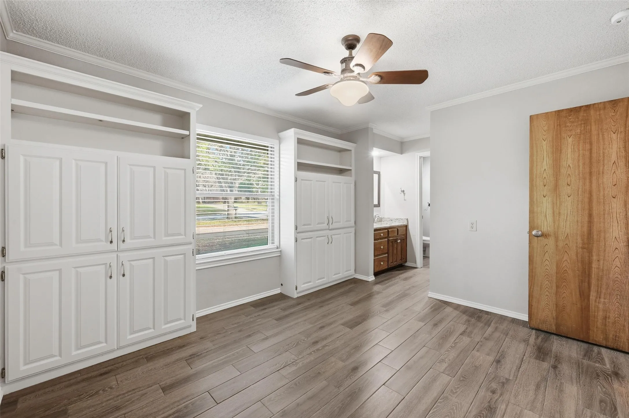 Unfurnished bedroom featuring crown molding, two closets, dark wood-type flooring, a textured ceiling, and a ceiling fan