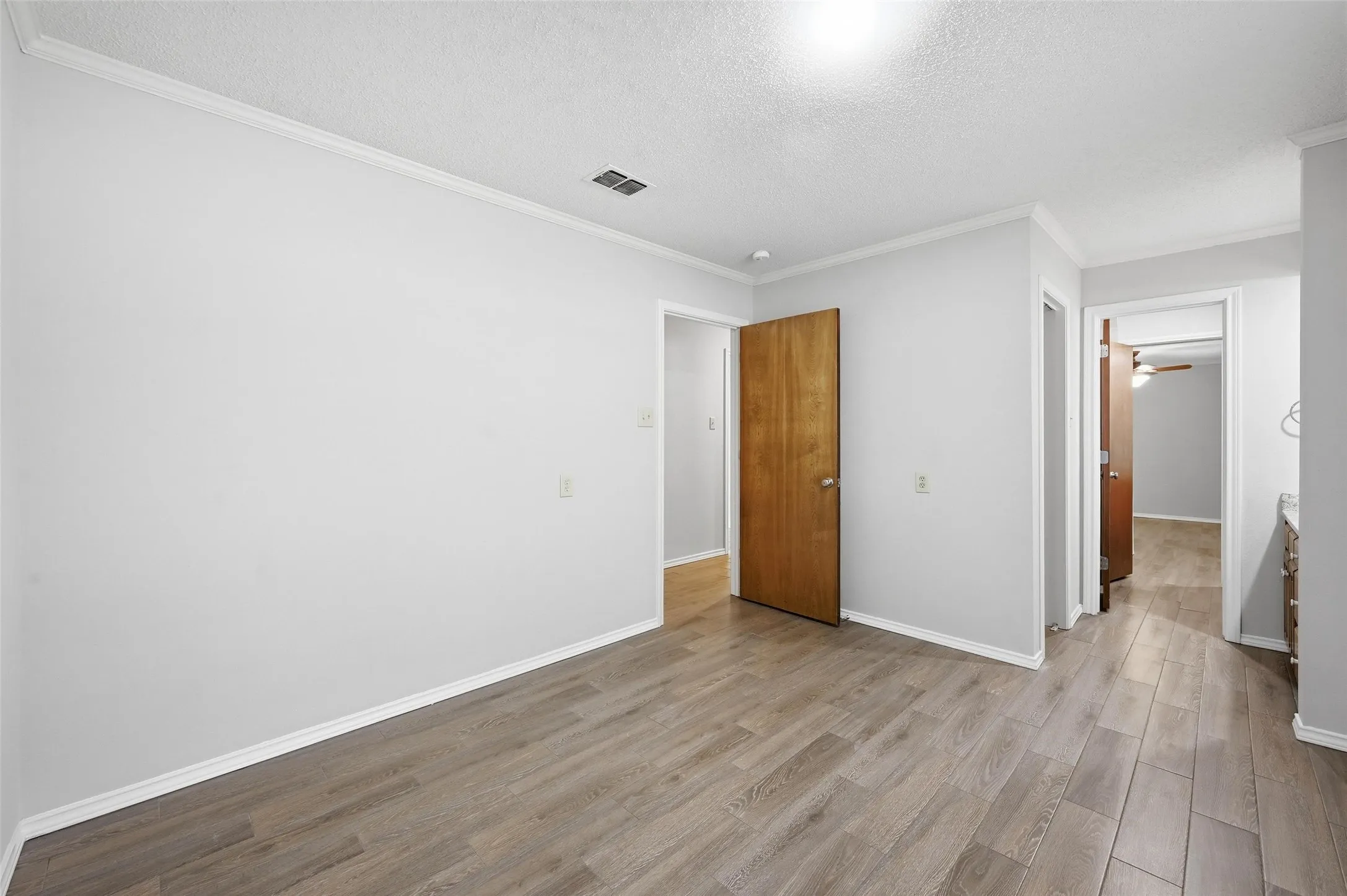 Unfurnished bedroom with light wood-type flooring, ornamental molding, and a textured​​‌​​​​‌​​‌‌​‌‌​​​‌‌​‌​‌​‌​​​‌​​ ceiling