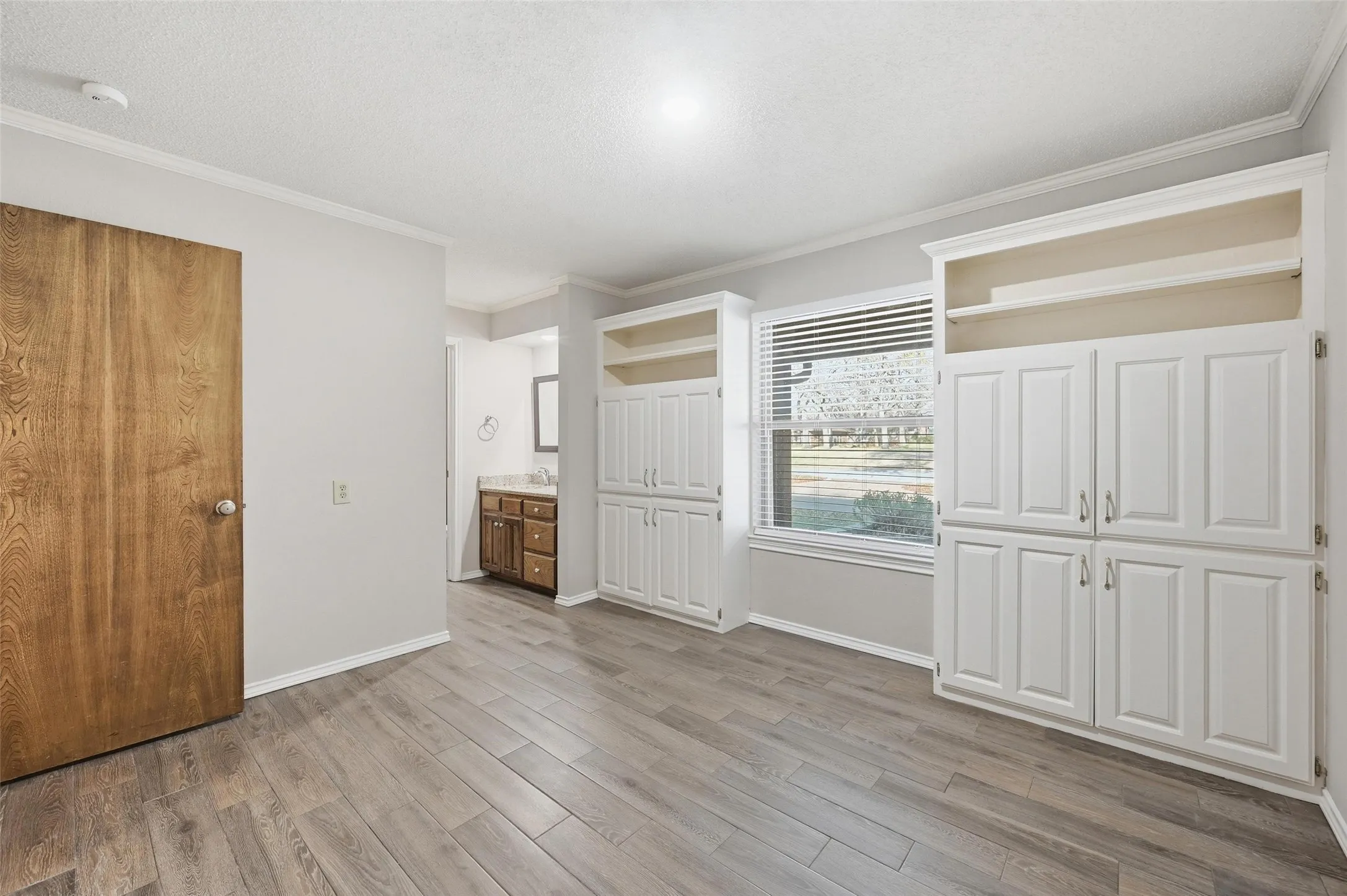 Unfurnished bedroom featuring ornamental molding, light wood-style flooring, a textured ceiling, and ensuite bathroom