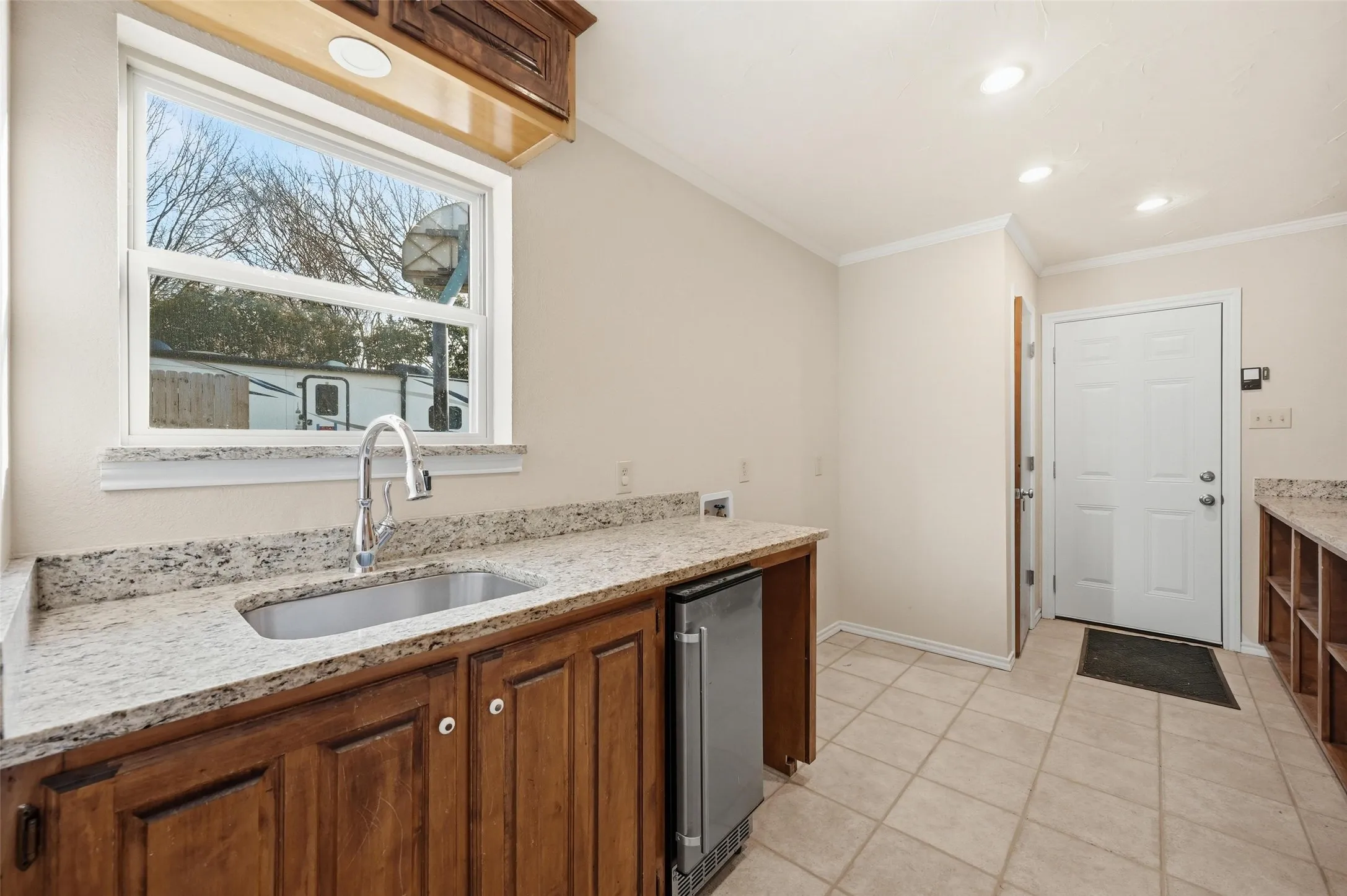 Utility Room with light stone counters, crown molding, light tile patterned flooring, stainless steel fridge, and wood finish cabinetry