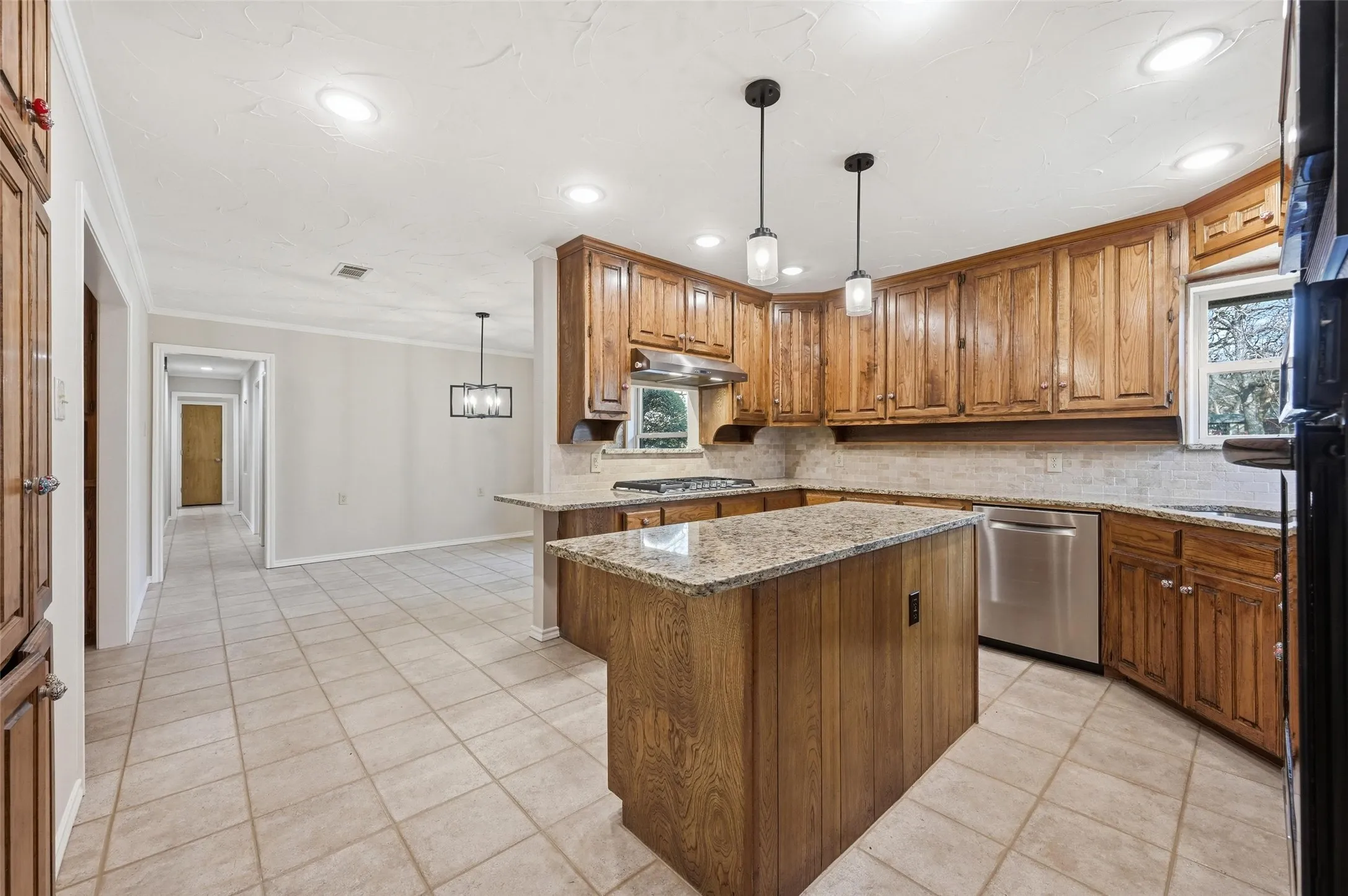 Kitchen with wood finish cabinetry, decorative light fixtures, light tile patterned flooring, ornamental molding, and a center island