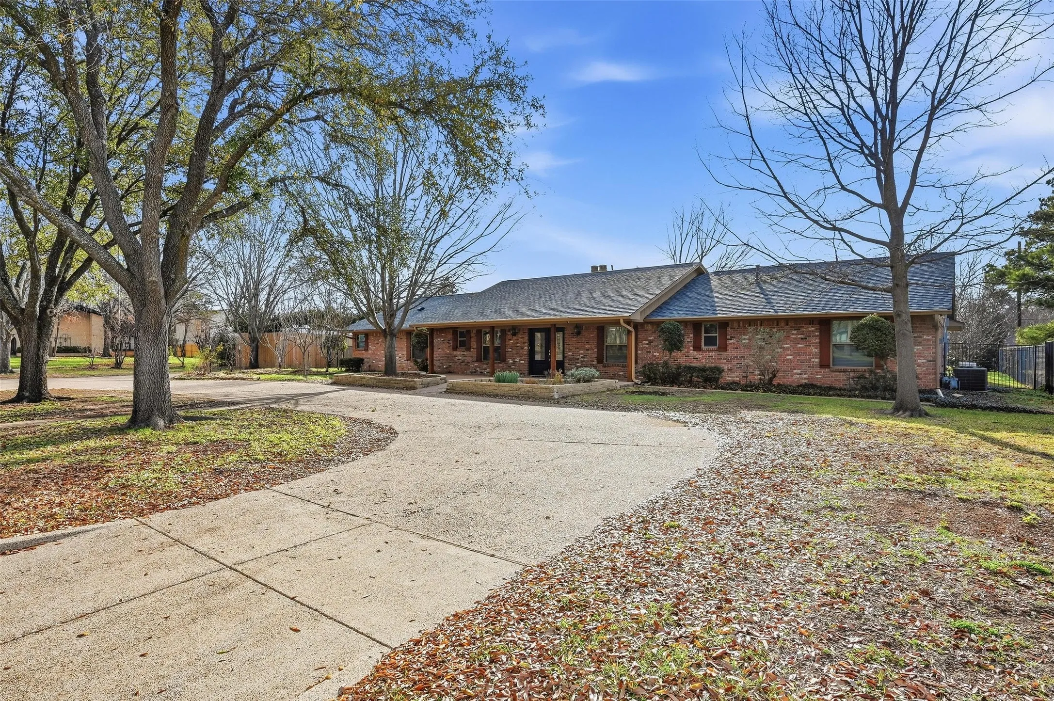 Ranch-style home with roof with shingles, curved driveway, brick siding, and covered porch