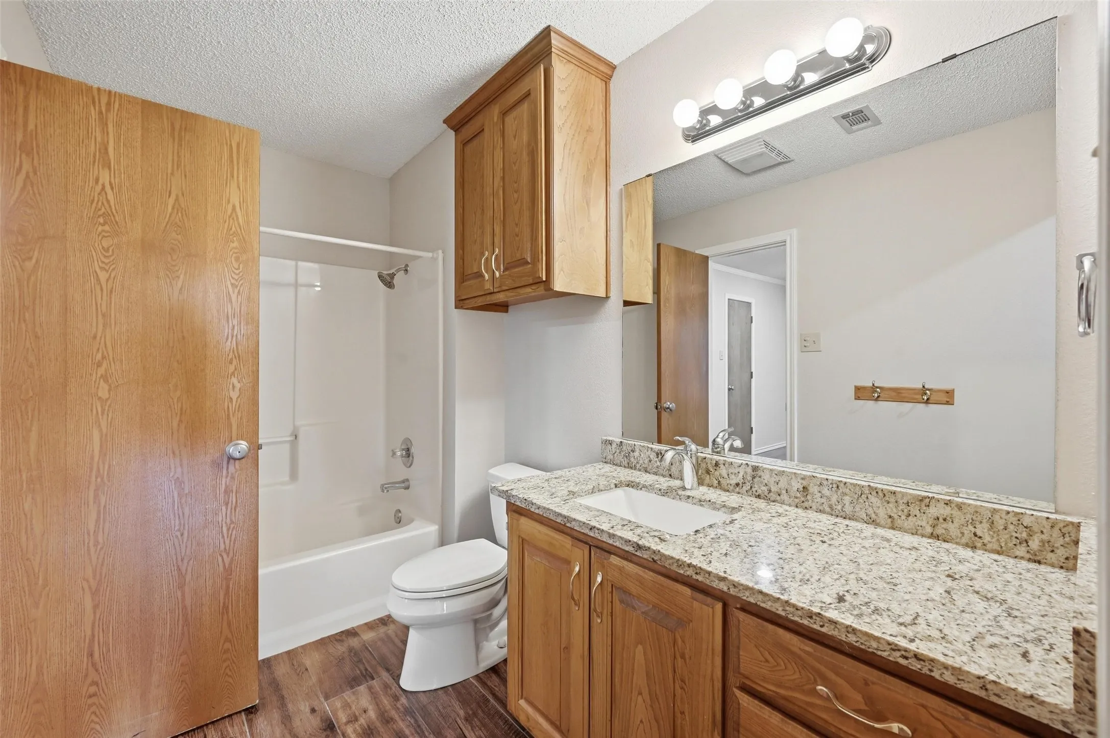Bathroom featuring vanity, a textured ceiling, dark wood-type flooring, and  shower combination