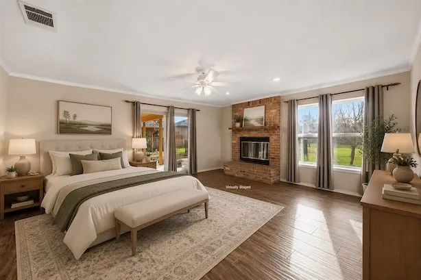 Spacious room featuring wood-finish flooring, a brick fireplace with a mantel, and multiple windows