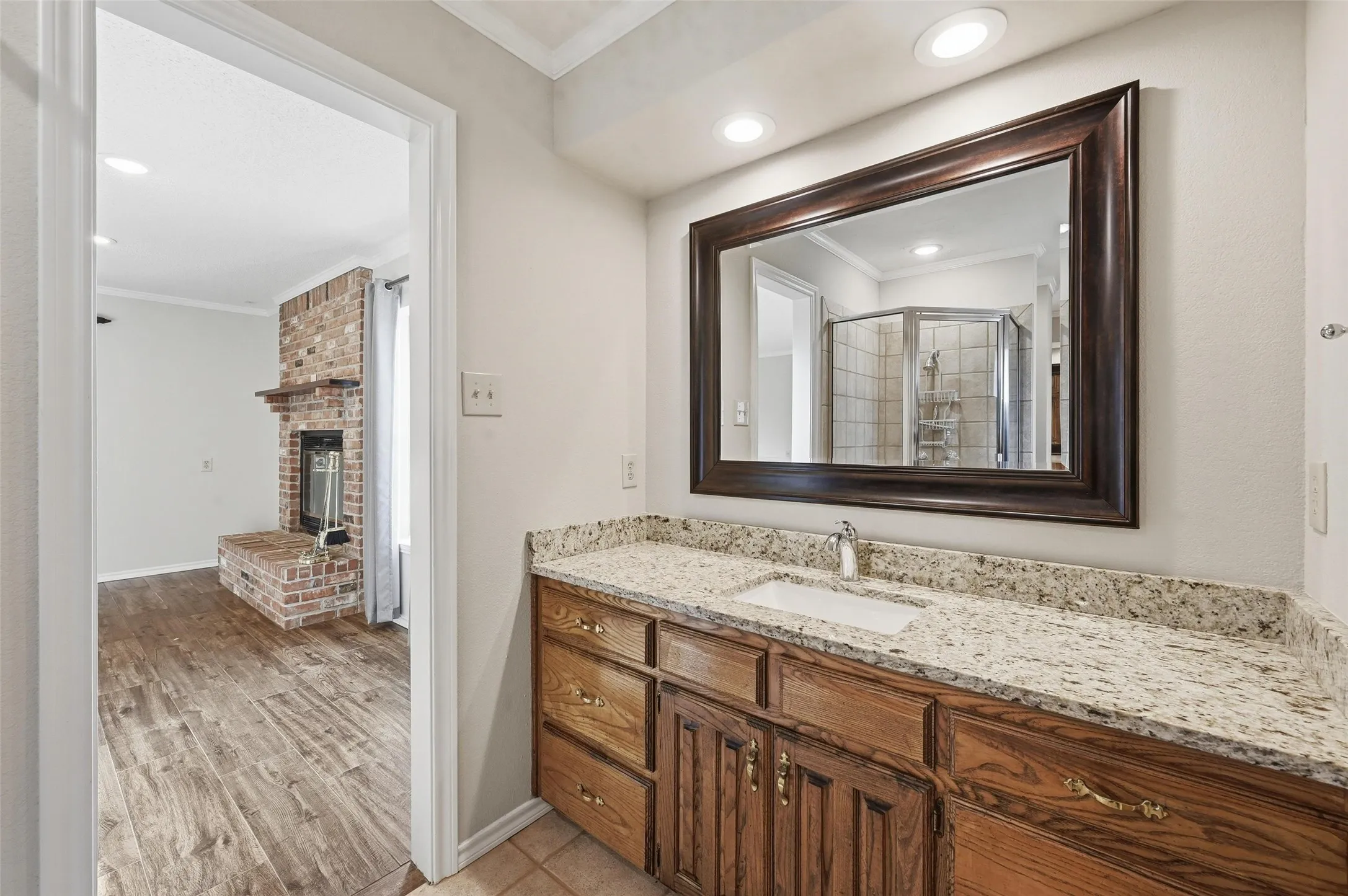 Bathroom with crown molding, vanity, light wood finished floors, a brick fireplace, and a shower stall