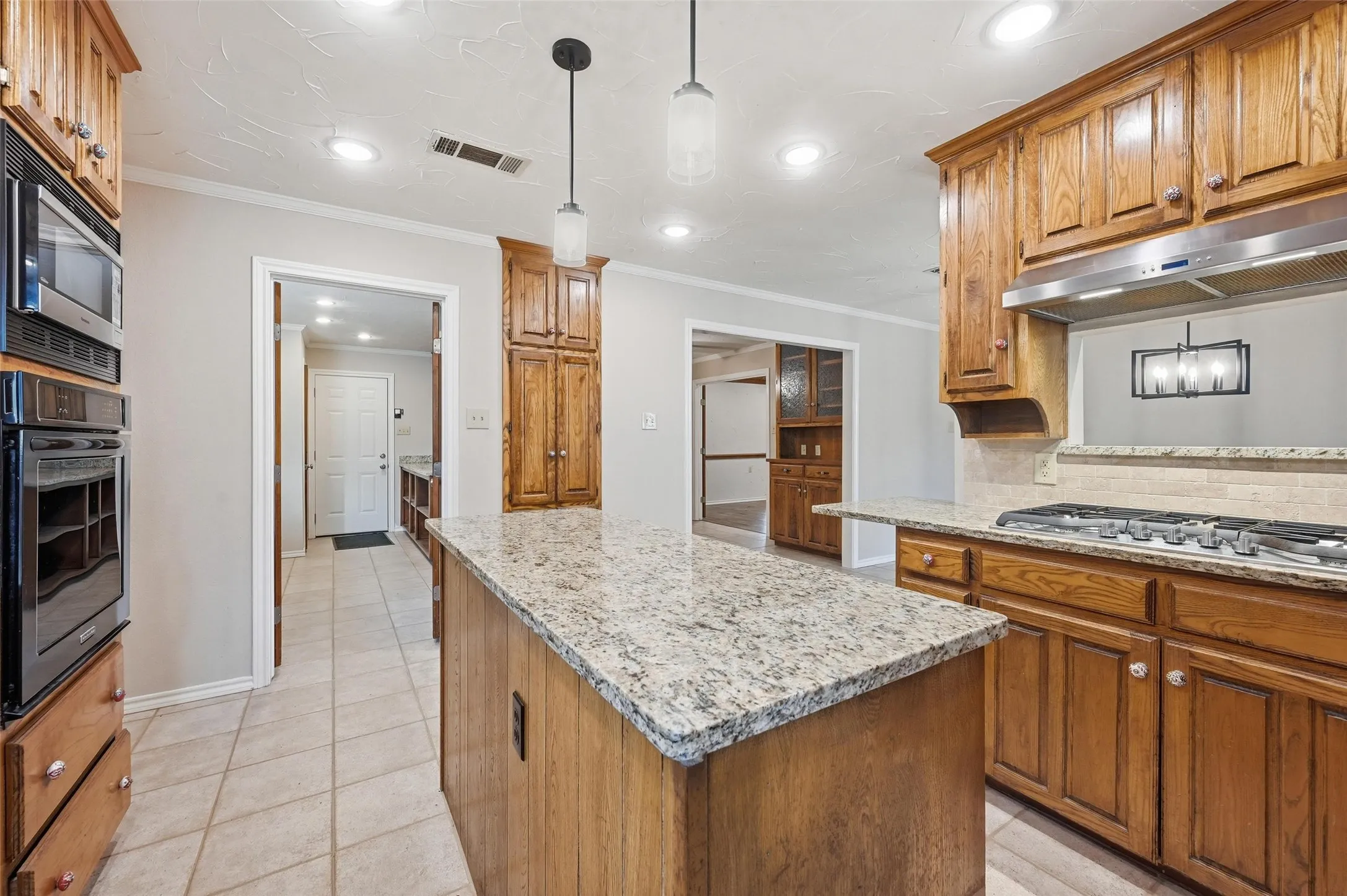Kitchen featuring wood finish cabinets, light stone counters, hanging light fixtures, and crown molding