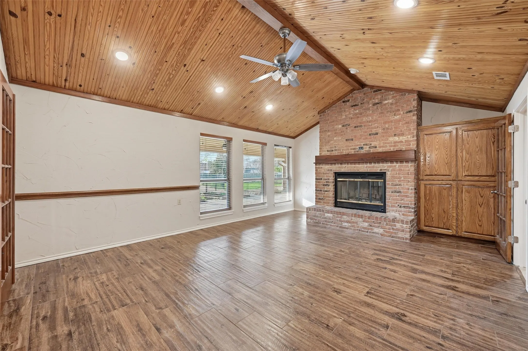 Unfurnished living room featuring a brick fireplace, ceiling fan, wood finished floors, and a wooden ceiling with exposed beams