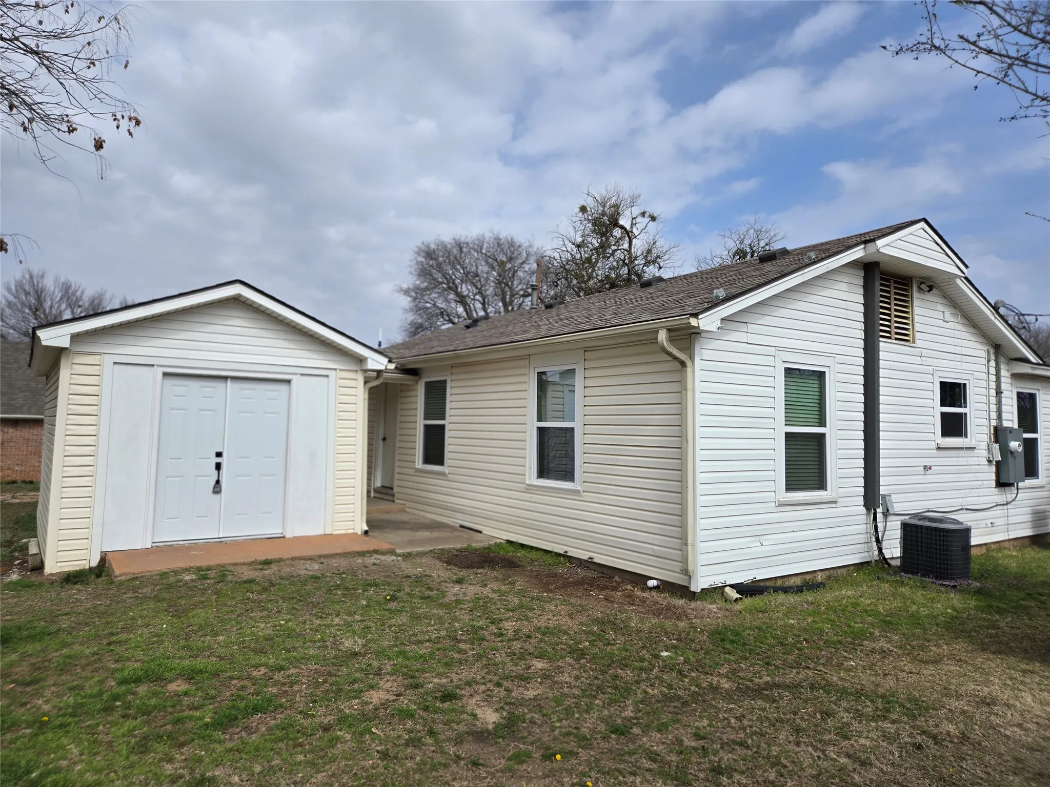 Rear view of property featuring a lawn, a storage shed, roof with shingles, and a patio
