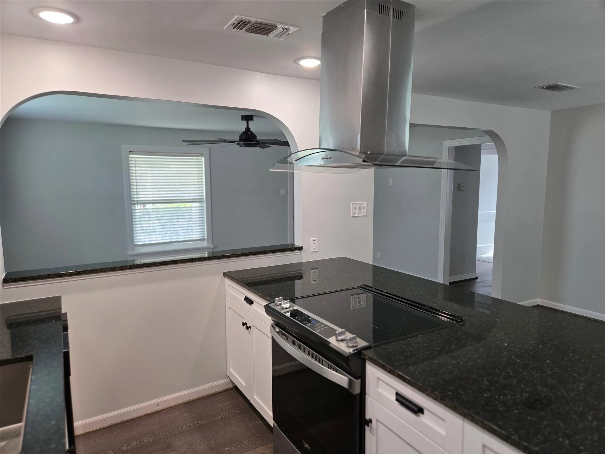 Kitchen with arched walkways, electric range oven, island range hood, dark stone counters, and a ceiling fan