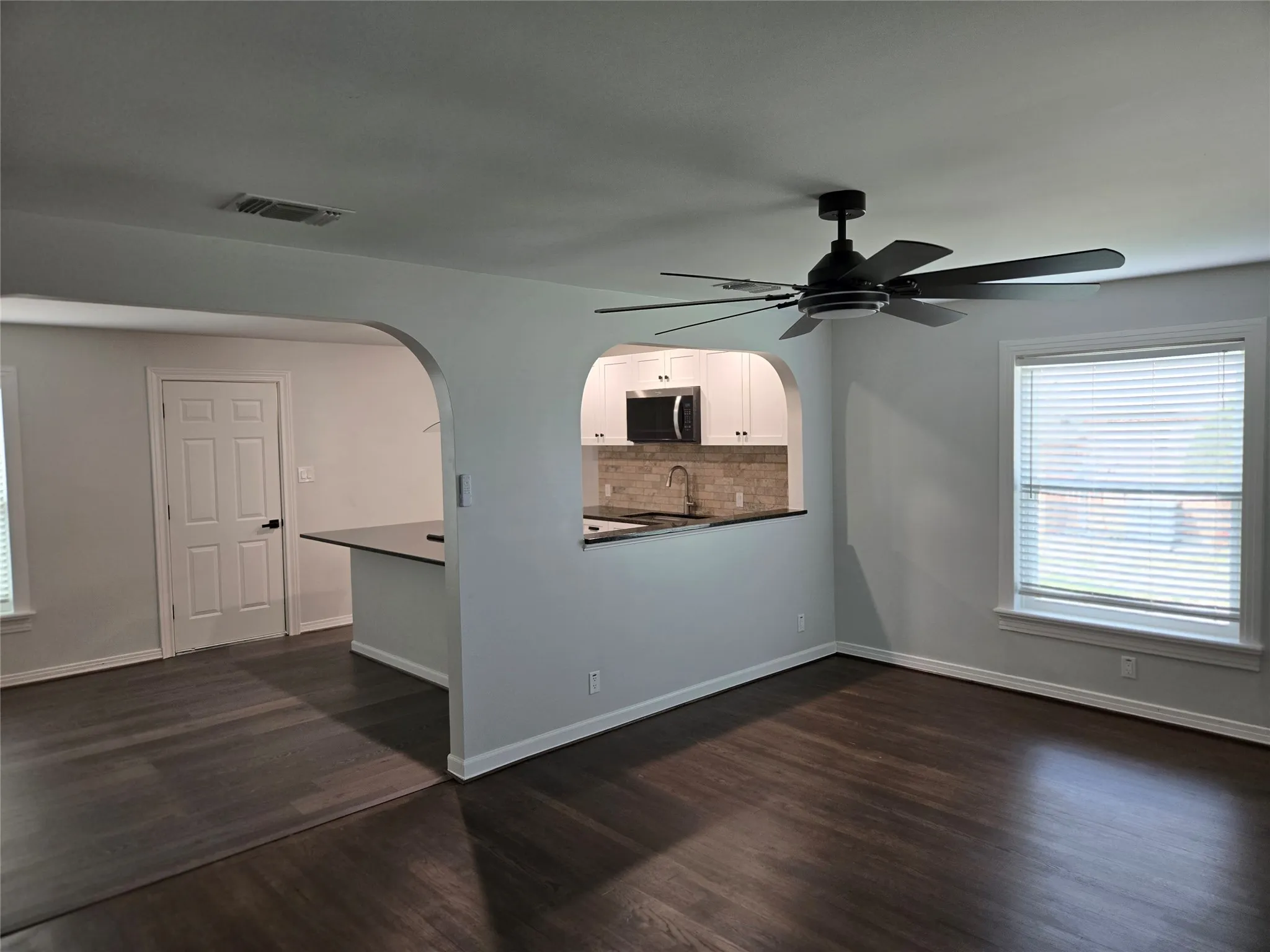 Empty room with arched walkways, dark wood-type flooring, and a ceiling fan