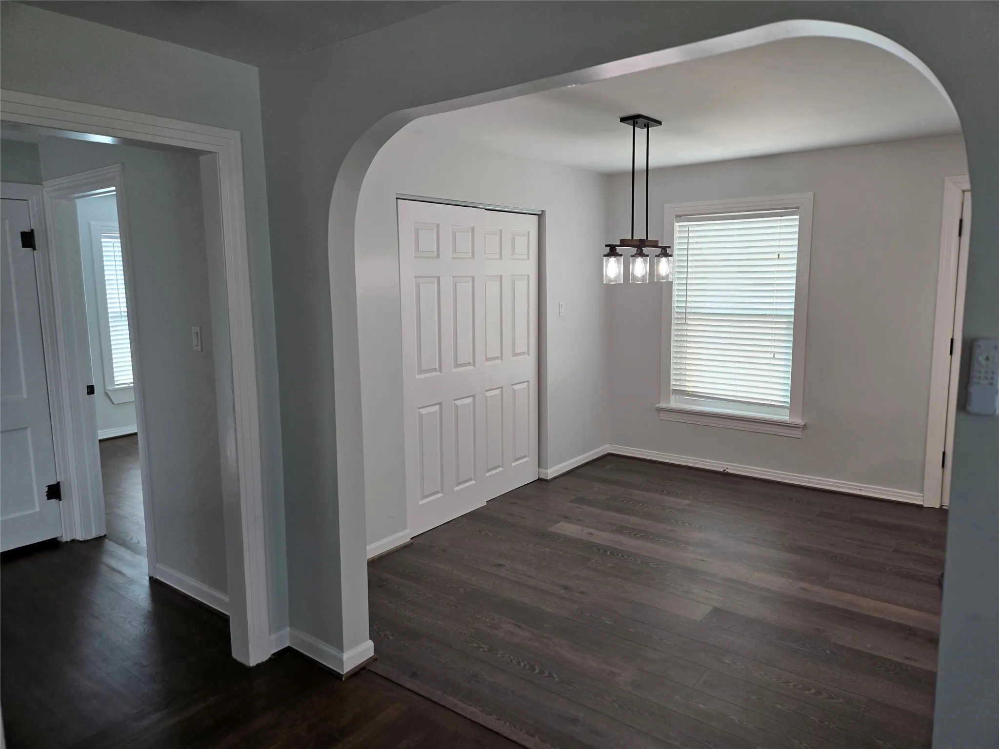 Unfurnished dining area featuring arched walkways, dark wood-style floors, and a chandelier