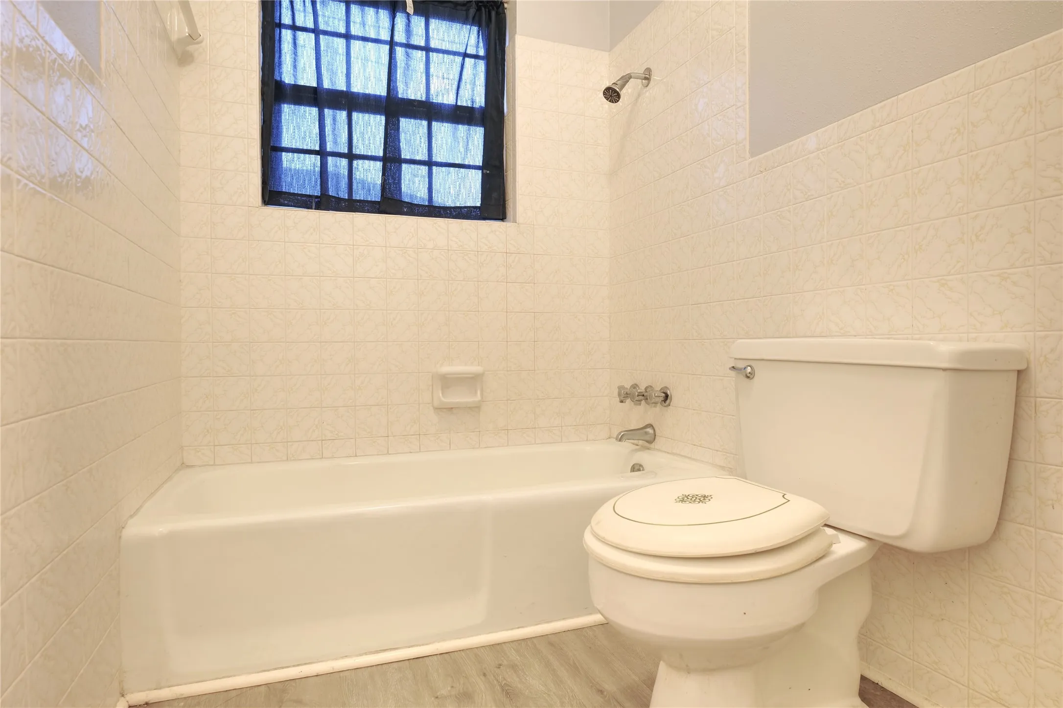 Bathroom featuring tile walls, shower / bath combination, and wood finished floors