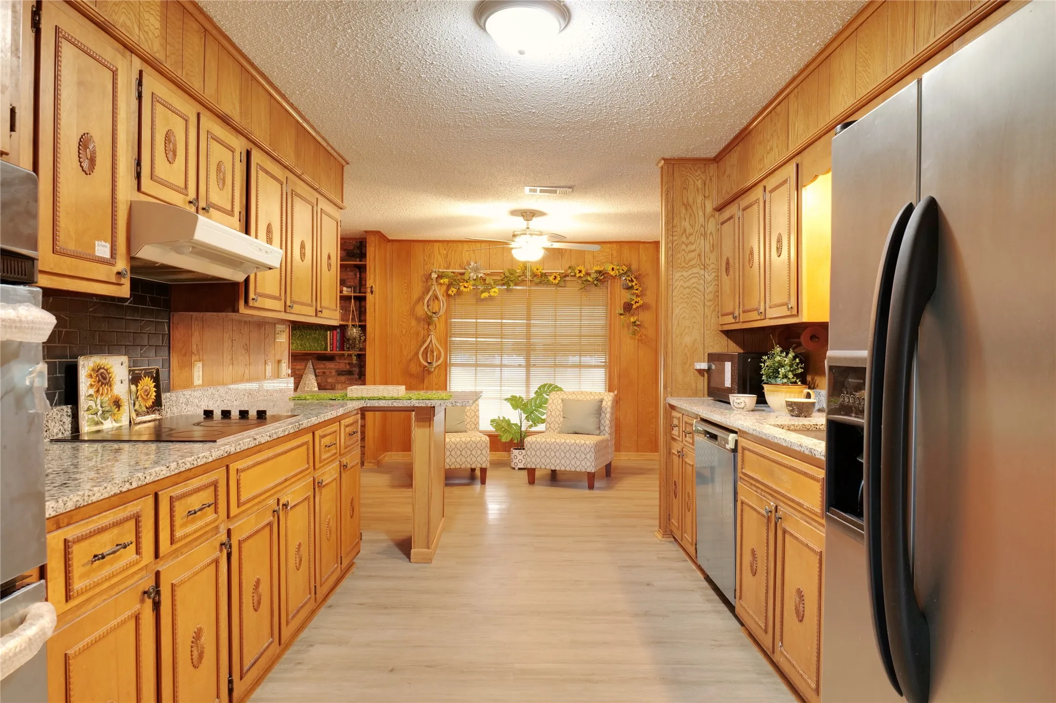Kitchen with stainless steel appliances, a textured ceiling, light stone counters, light wood-type flooring, and ceiling fan