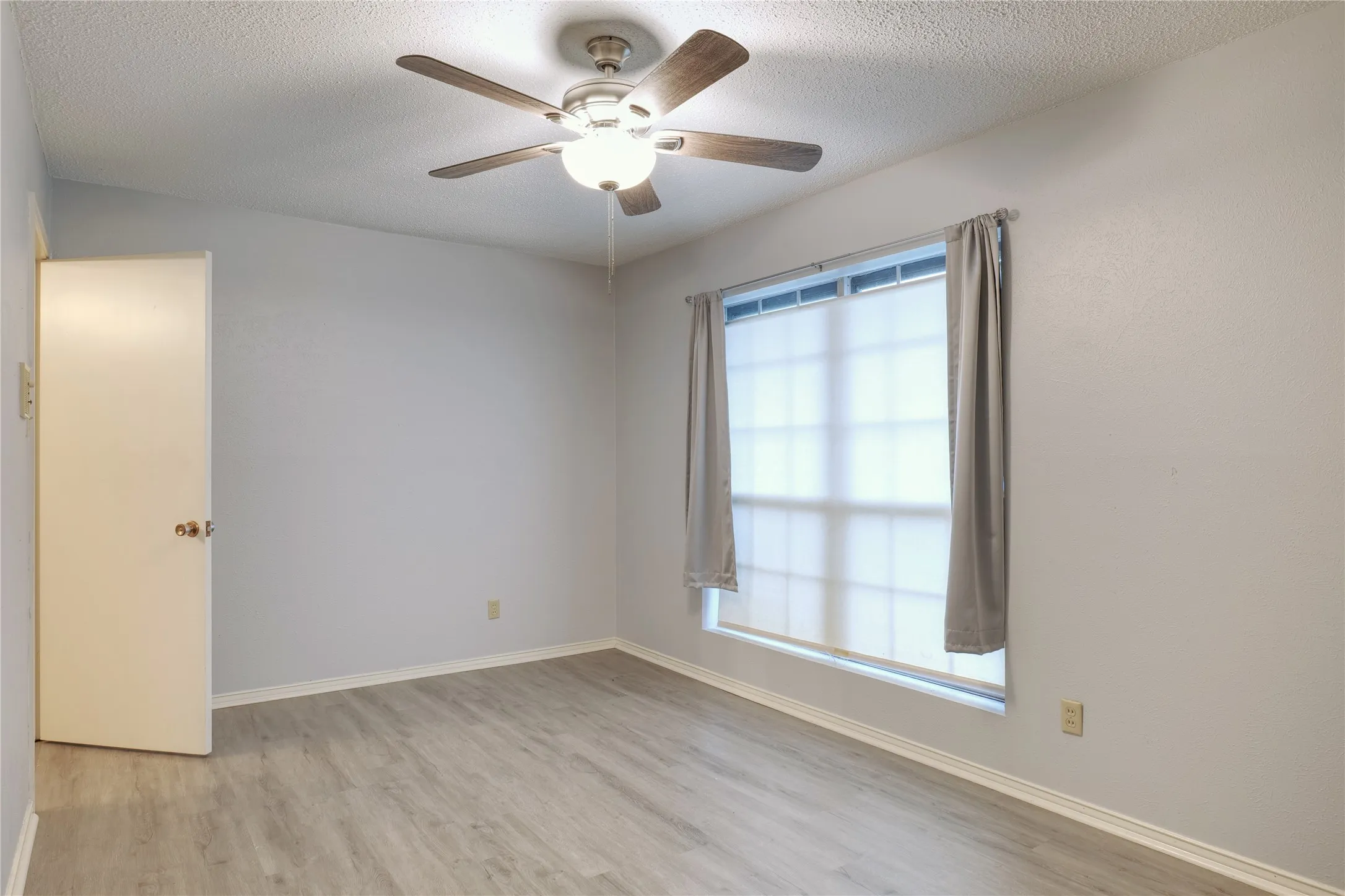 Empty room with ceiling fan, light wood-style floors, and a textured ceiling
