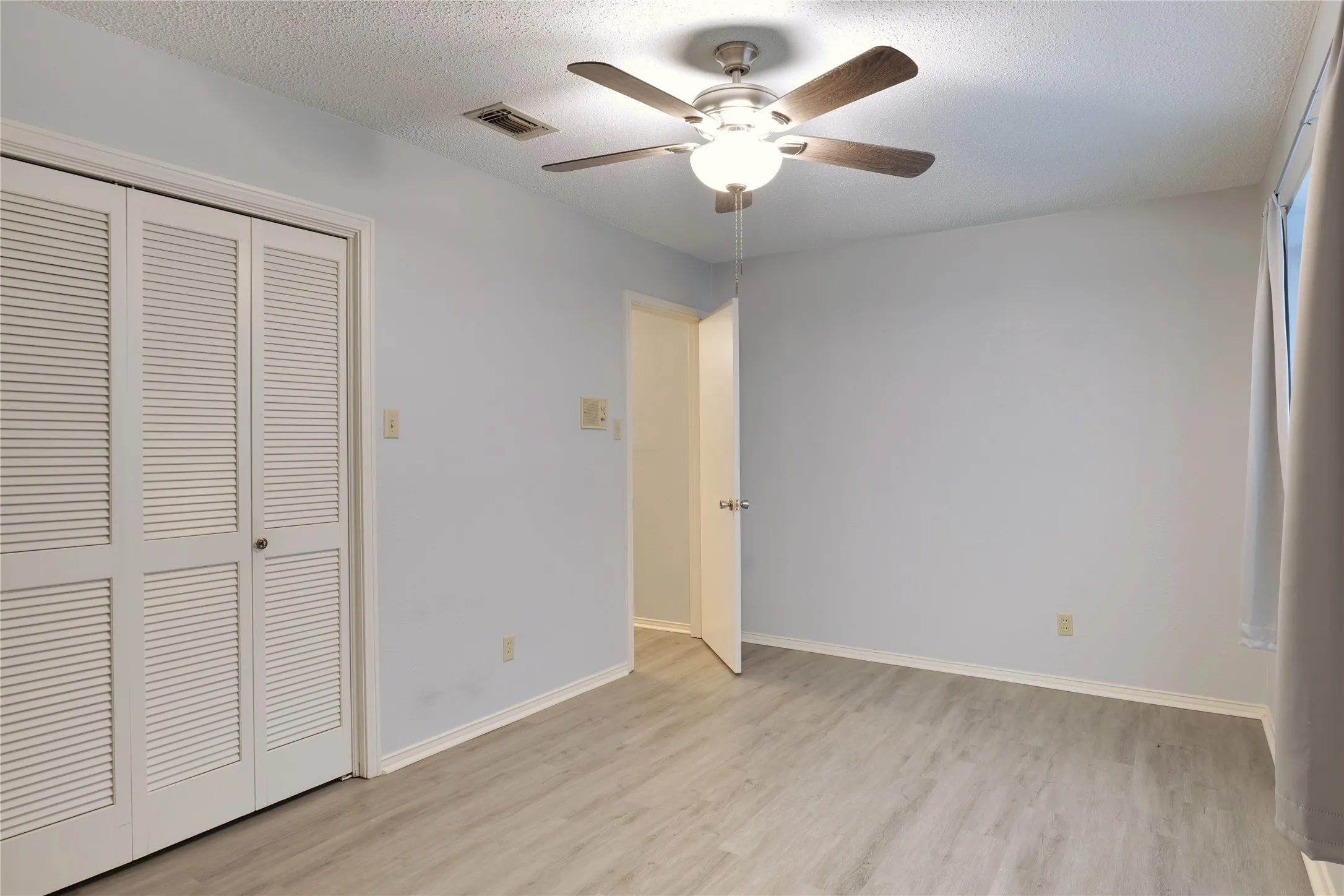Unfurnished bedroom featuring ceiling fan, light wood-type flooring, a textured ceiling, and a closet