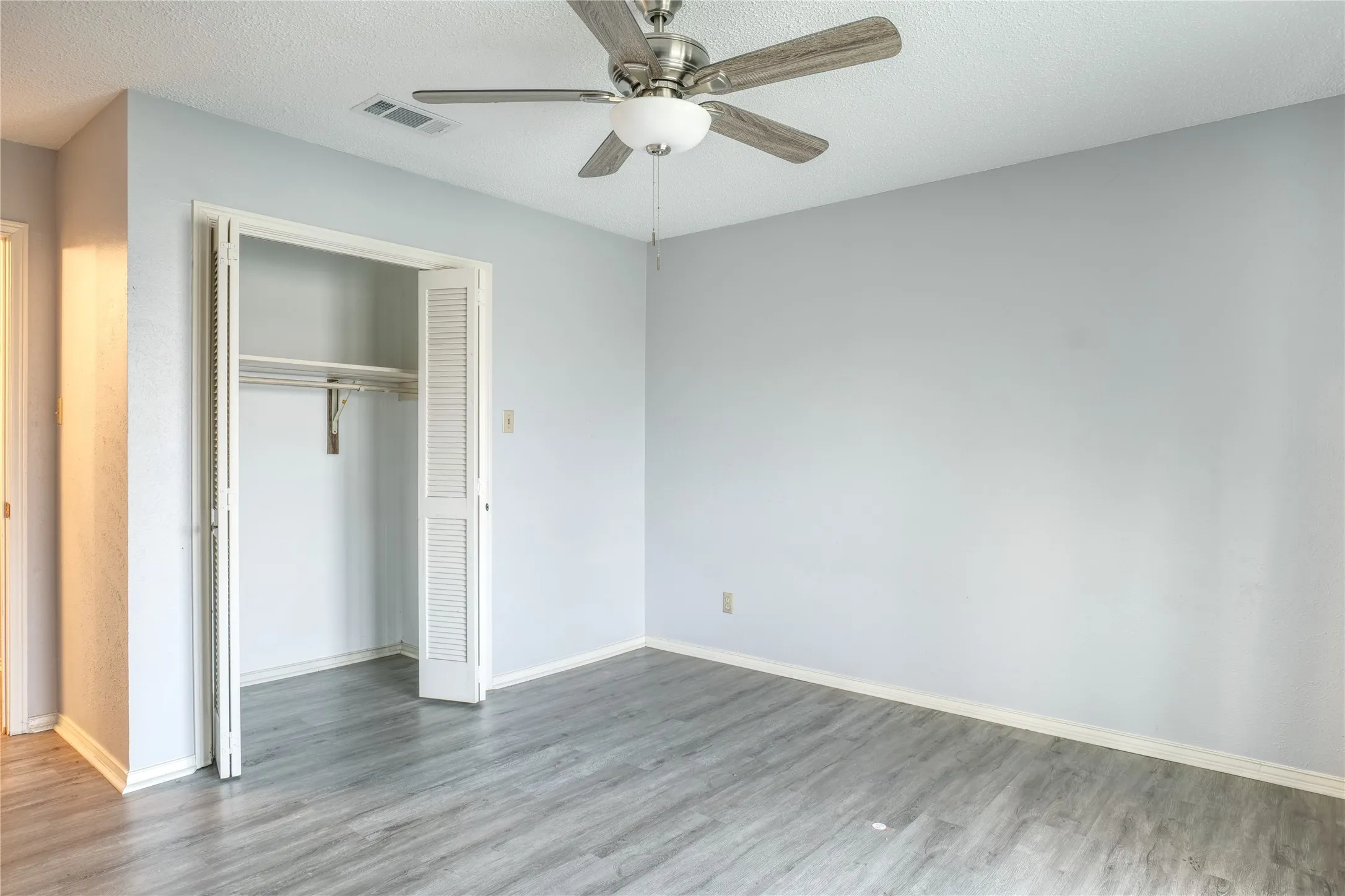 Unfurnished bedroom featuring a closet, a textured ceiling, a ceiling fan, and wood finished floors