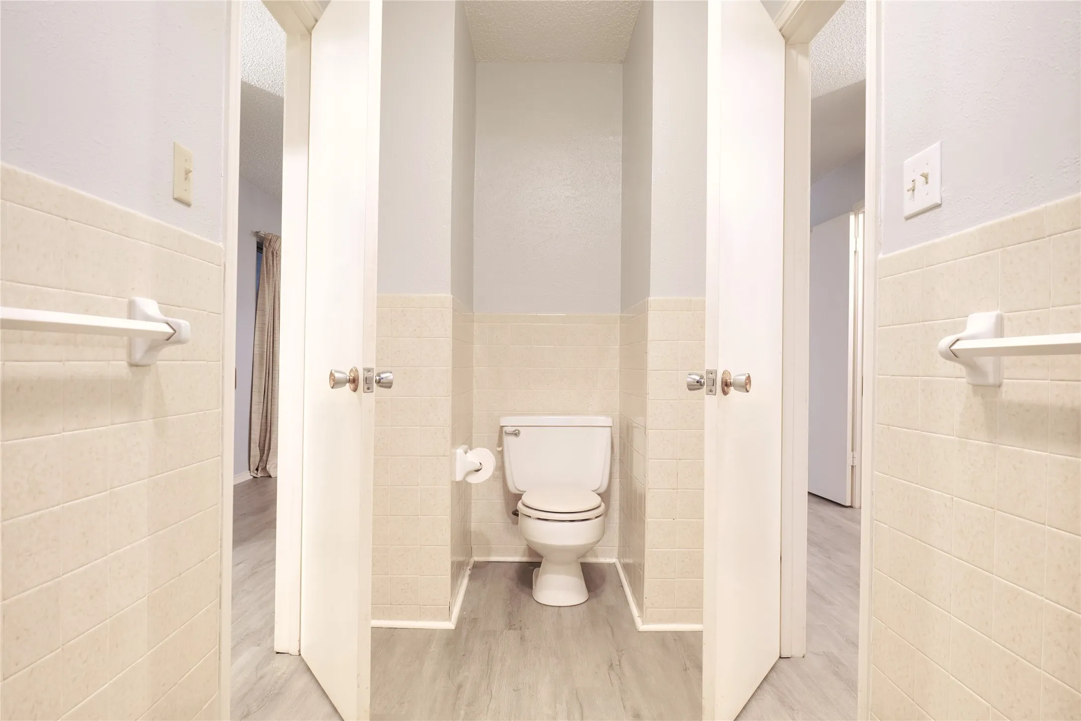 Bathroom with tile walls, wainscoting, light wood-style flooring, and a textured ceiling