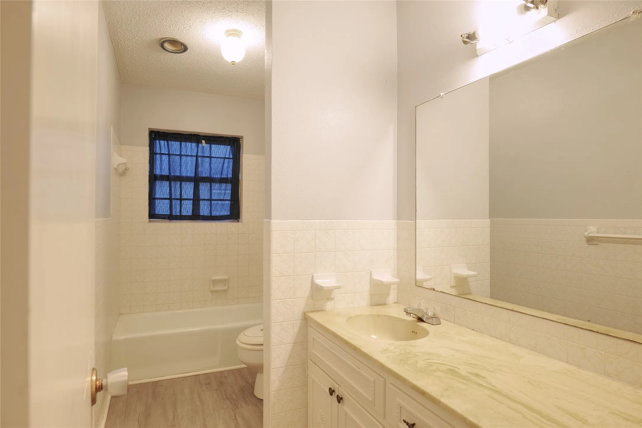Bathroom featuring vanity, tile walls, a textured ceiling, light wood finished floors, and bathing tub / shower combination