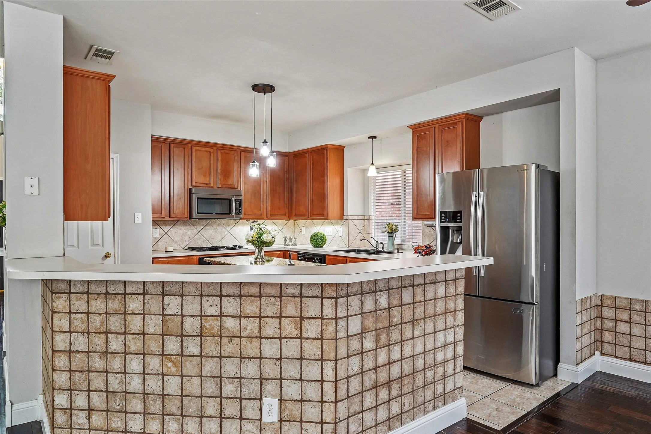 Kitchen featuring stainless steel appliances, light countertops, decorative backsplash, and wood finish cabinets