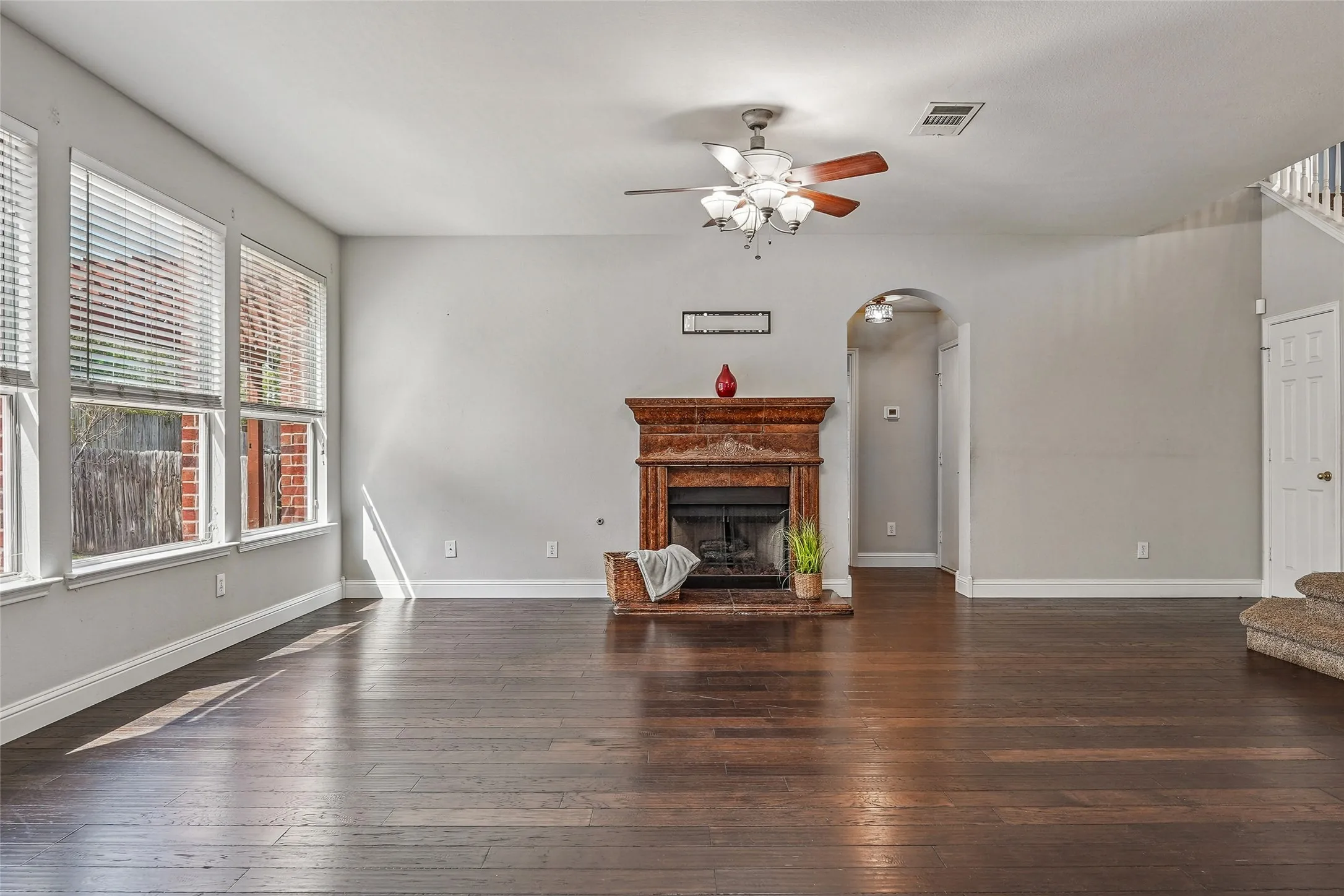 Unfurnished living room featuring dark wood-type flooring, a fireplace with raised hearth, ceiling fan, and arched walkways