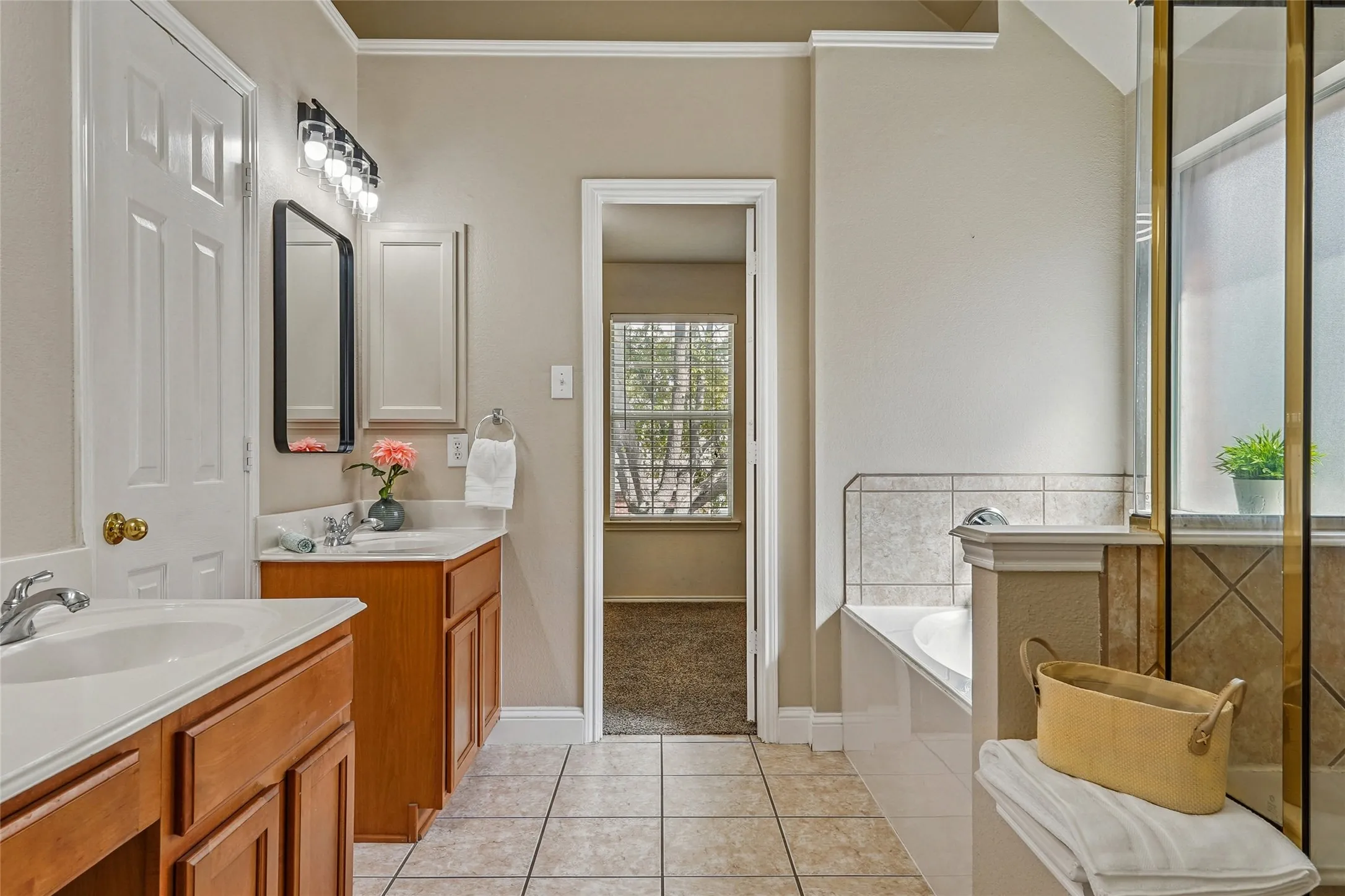 Bathroom featuring two vanities, light tile patterned floors, a bath, and ornamental molding