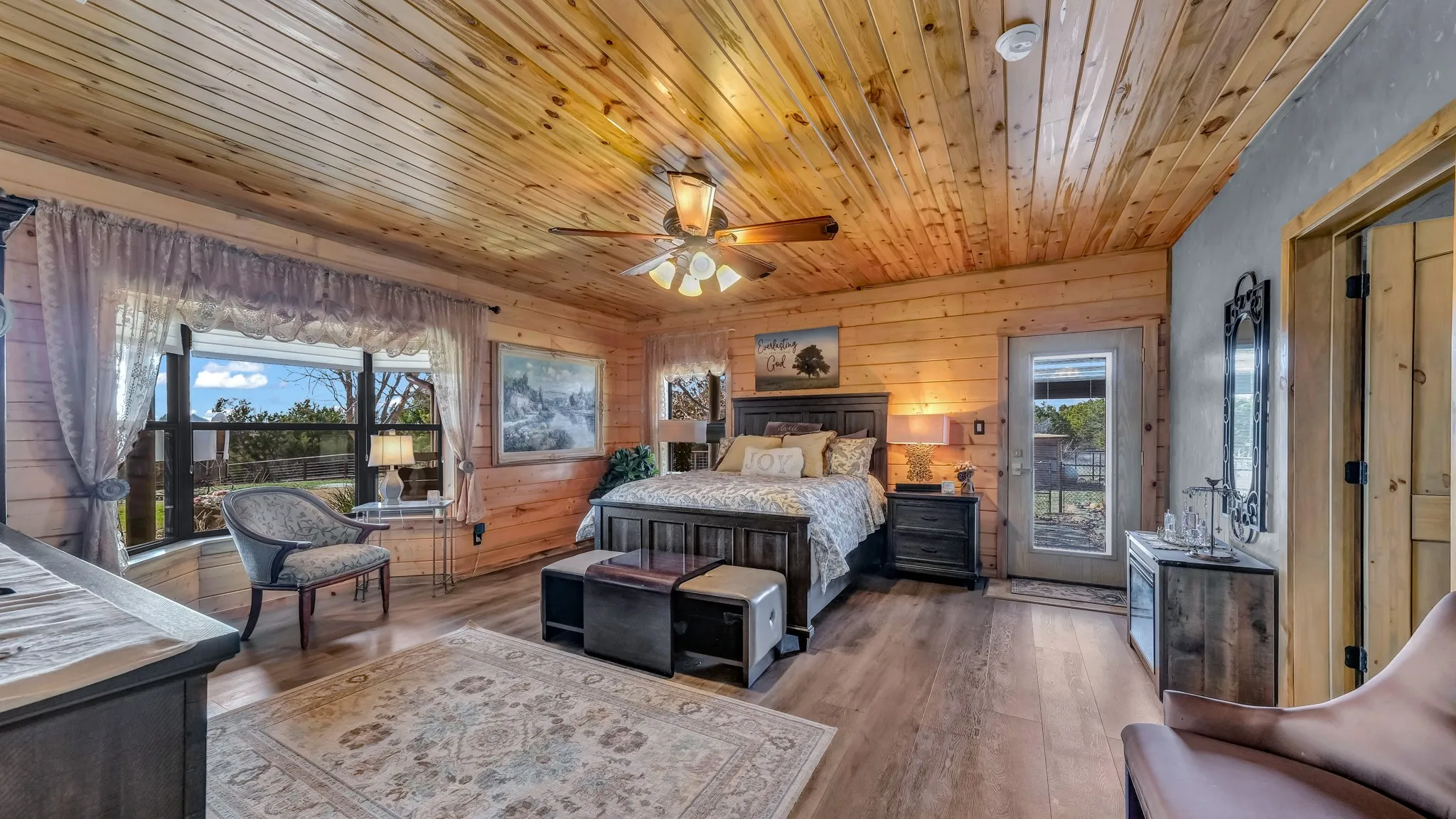 Primary oversized bedroom downstair is a serene sanctuary for escape.  Notice the bay window, blue plne ceilings, vinyl plank flooring and door to the outside patio.