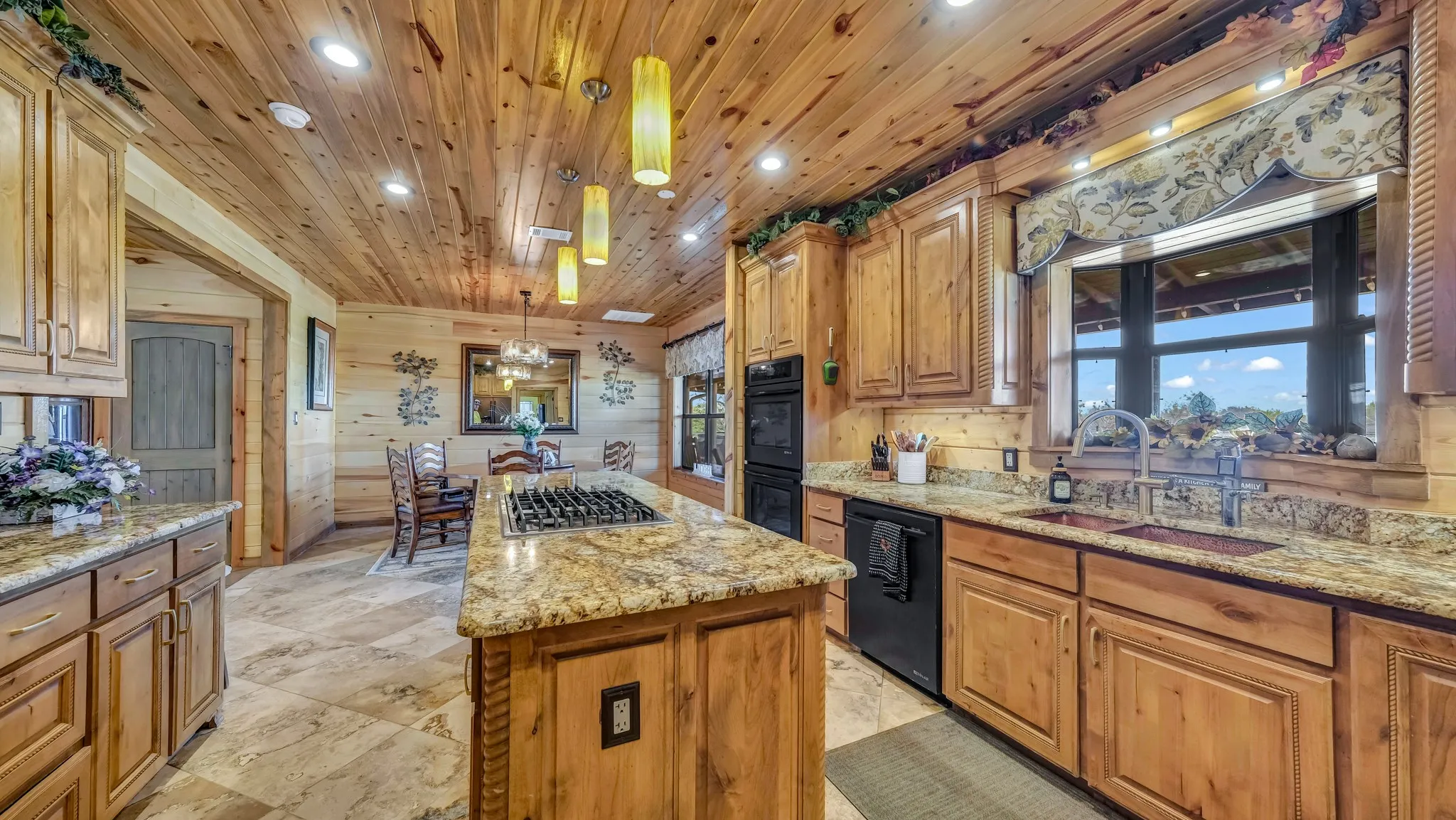 Kitchen has a large center island, granite countertops, gas cooktop, handmade knotty alder cabinets, blue pine ceilings, bay window,coppoer sinks,  and travertine flooring.