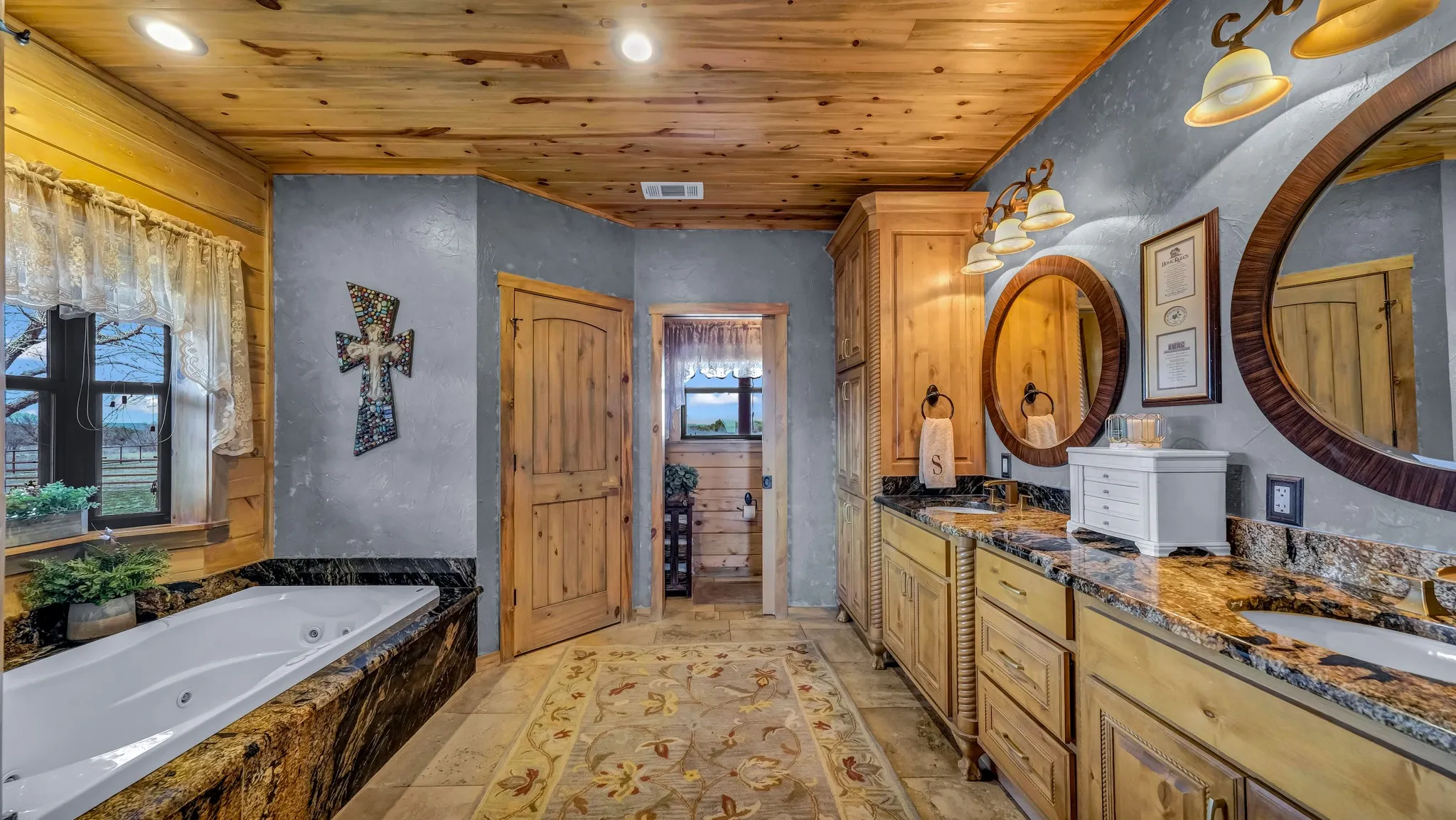 Ensuite master bathroom has a large jetted jacuzzi tub, bay window, separate toilet and shower area, two separate sinks, and travertine flooring.