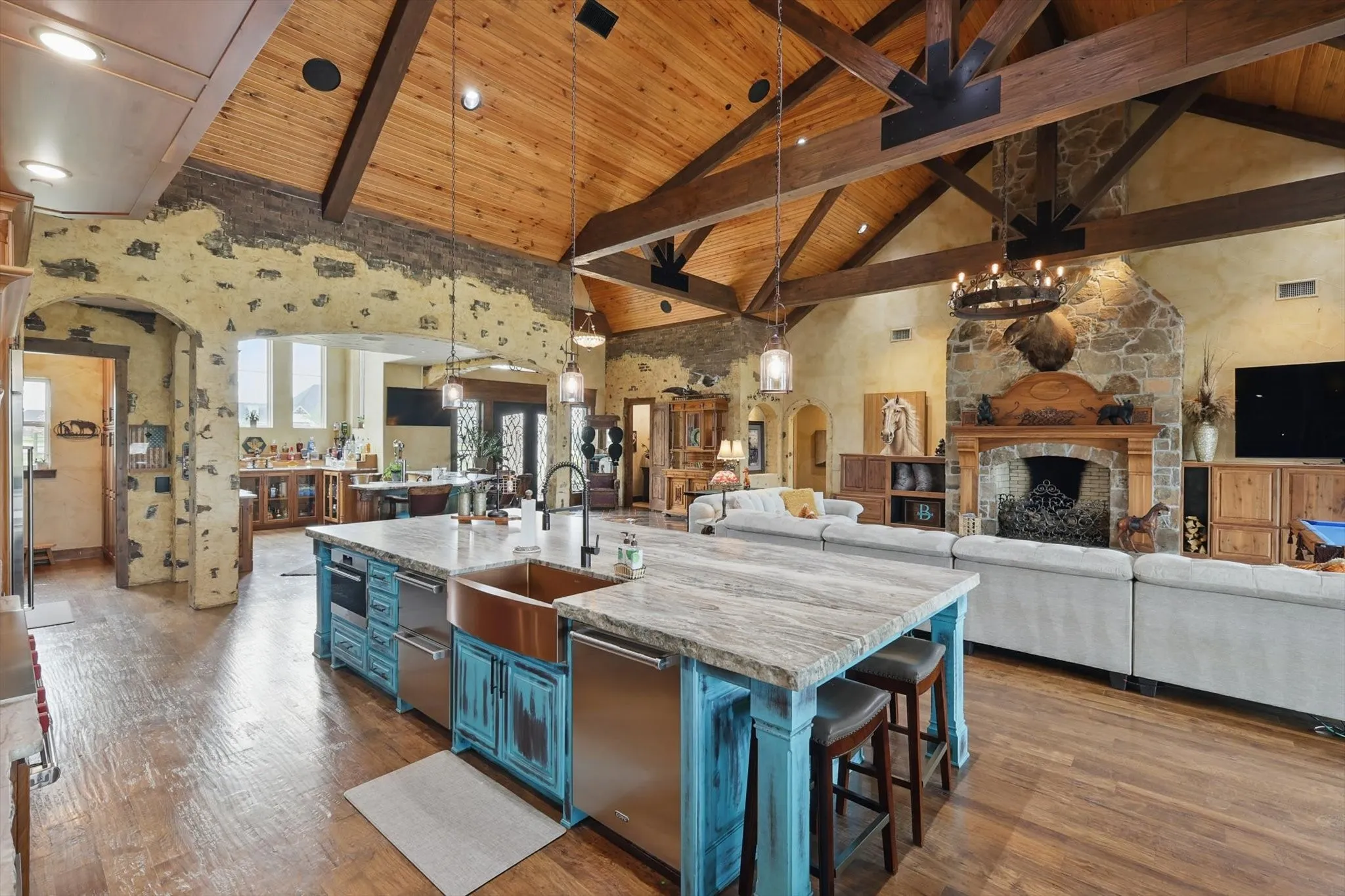 Kitchen with open floor plan, blue cabinetry, arched walkways, a high wood beamed ceiling, and light stone counters