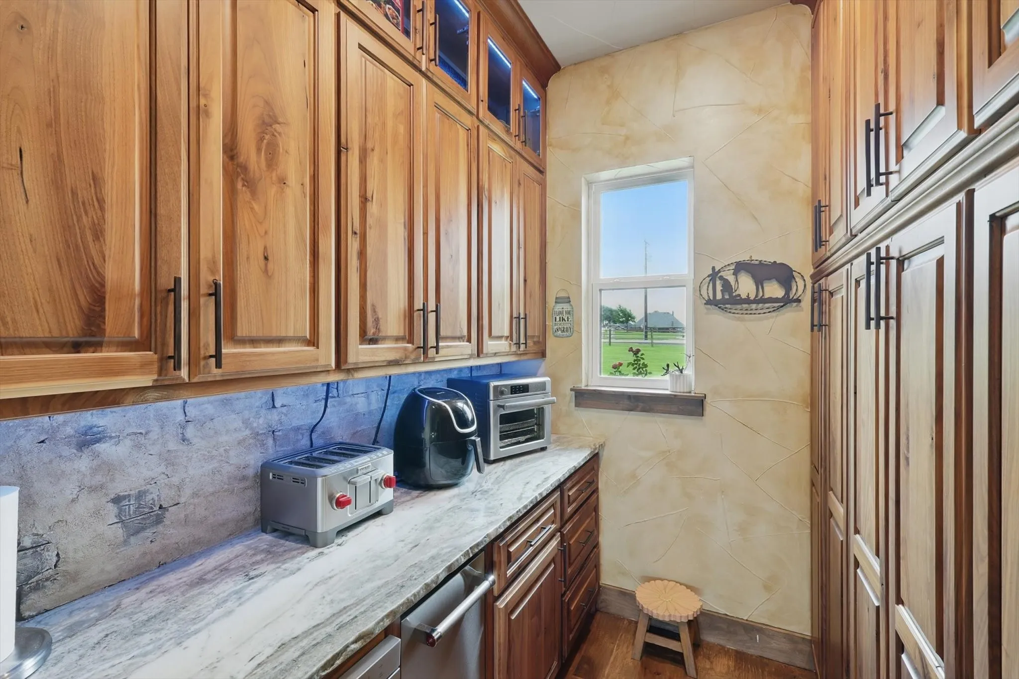 Kitchen featuring light stone counters, wood finish cabinetry, glass fronted cabinets, decorative backsplash, and stainless steel dishwasher