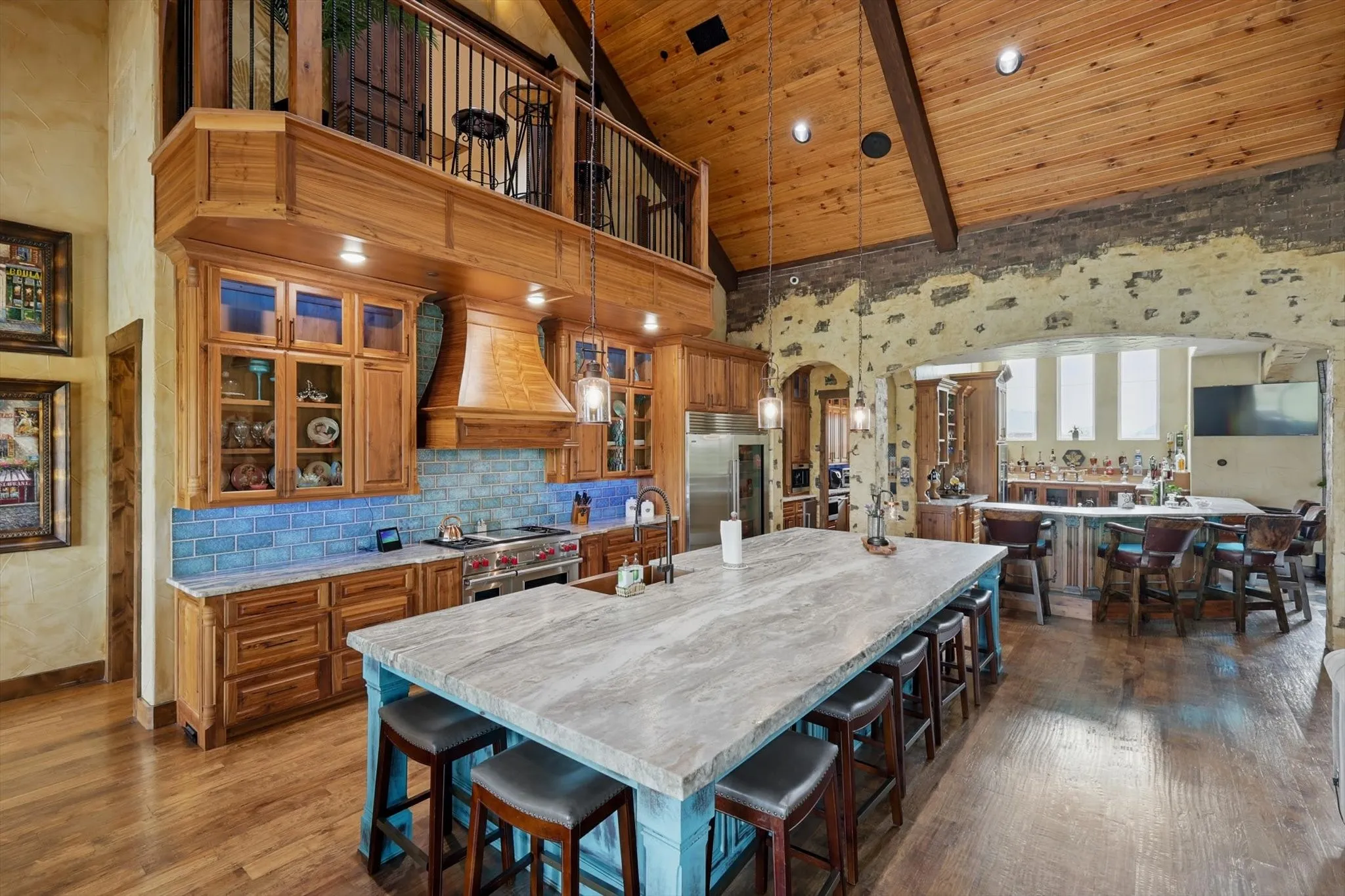 Kitchen with arched walkways, wood finish cabinetry, a large island with sink, a kitchen breakfast bar, and a vaulted wooden ceiling