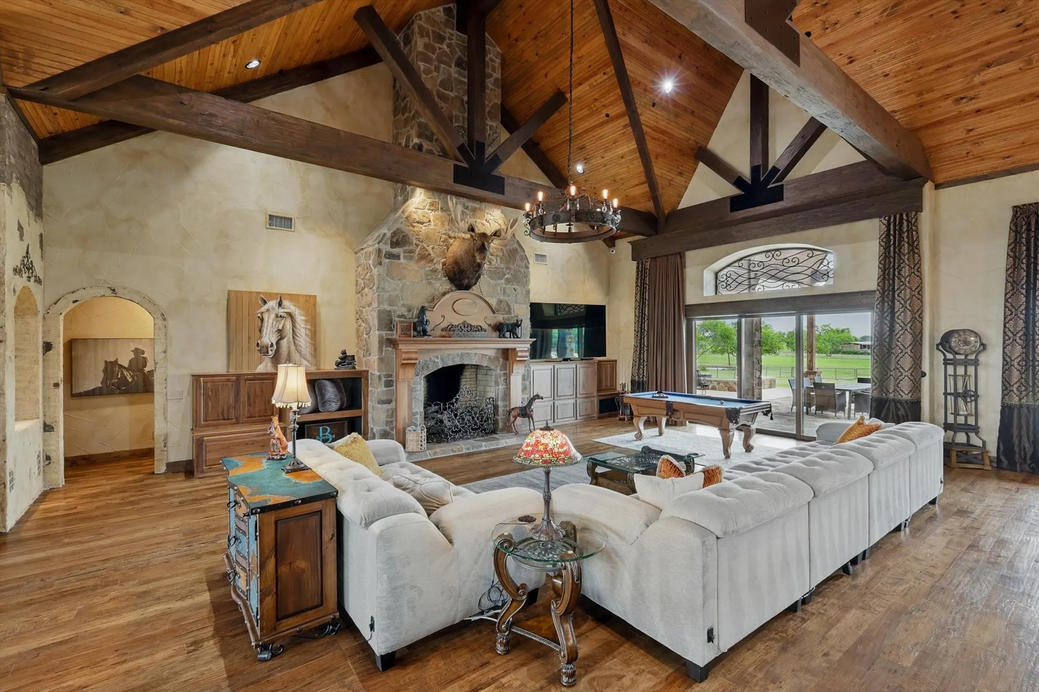Living room with a fireplace, arched walkways, pool table, suspended lighting, and a high wooden beamed ceiling